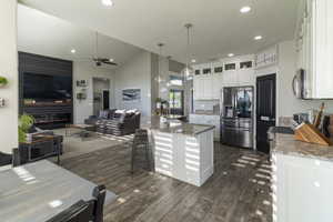 Open-concept living space featuring vaulted ceilings, wood-finish flooring, a kitchen island with pendant lighting, white cabinetry, and stainless steel appliances