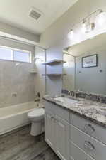 Updated bathroom featuring a single vanity with stone-finish countertop, undermount sink, and light wood-finish flooring