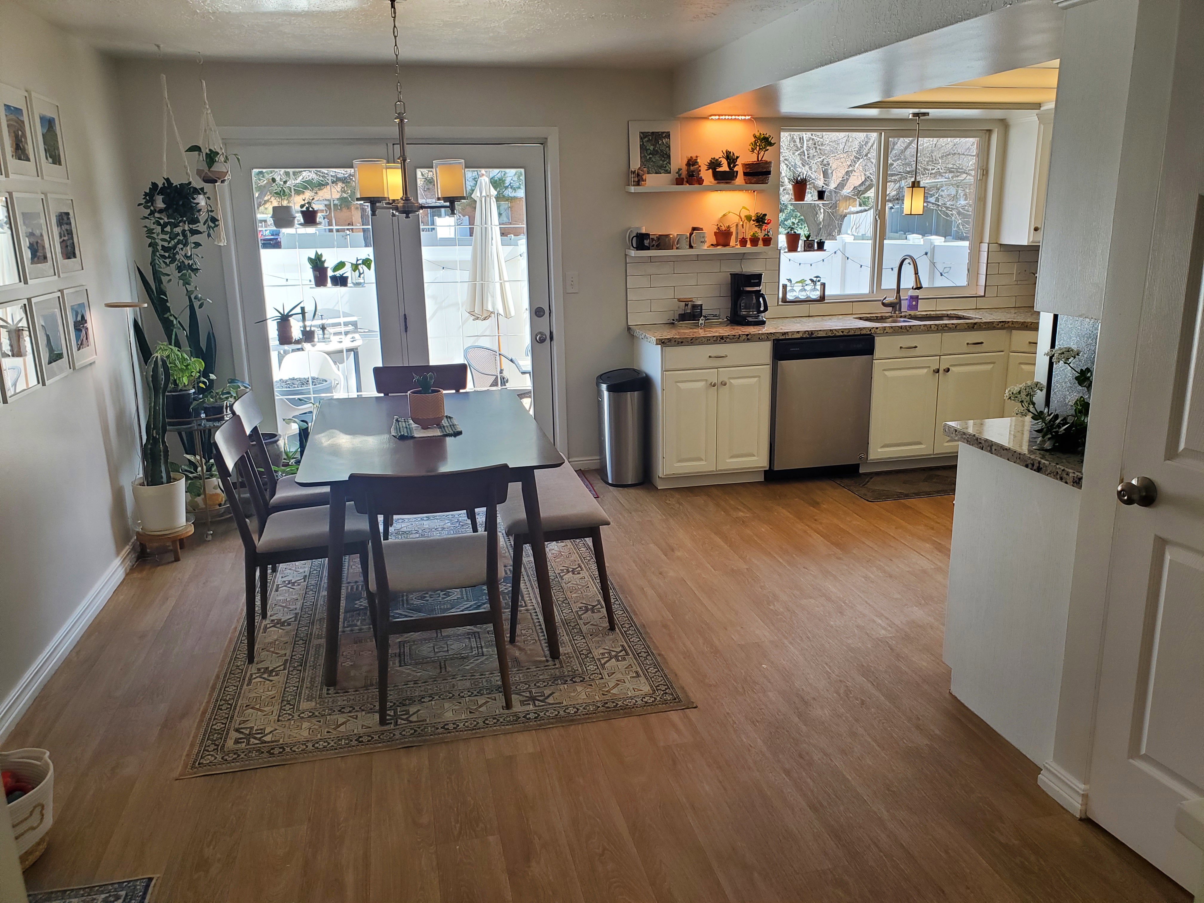 Open-concept living space featuring wood-finish flooring, a kitchen with white cabinetry and light-toned countertops, and a dining area with direct outdoor access via double glass doors