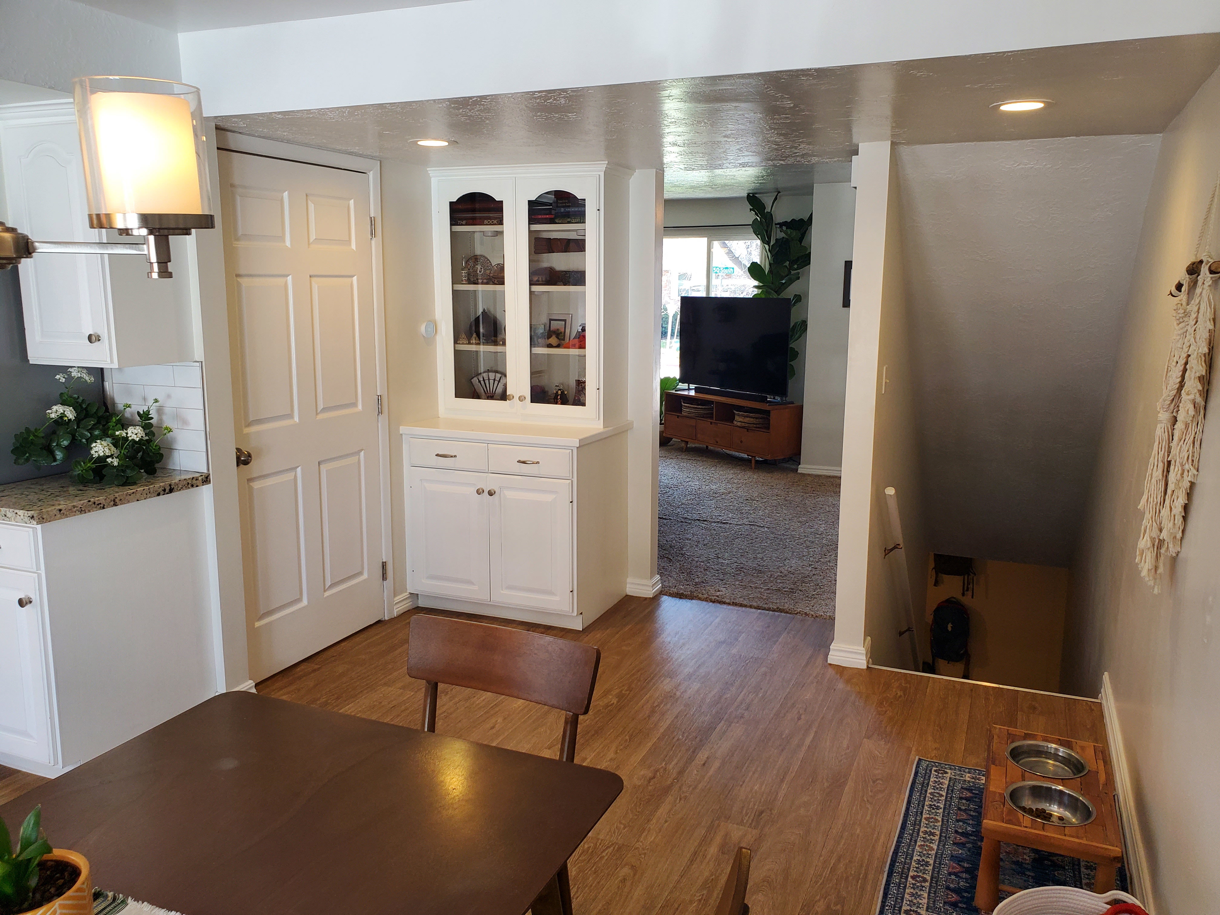 Hardwood-finish flooring extending from the dining area to a lower level, complemented by a built-in white display cabinet with glass-fronted upper doors and a functional white door