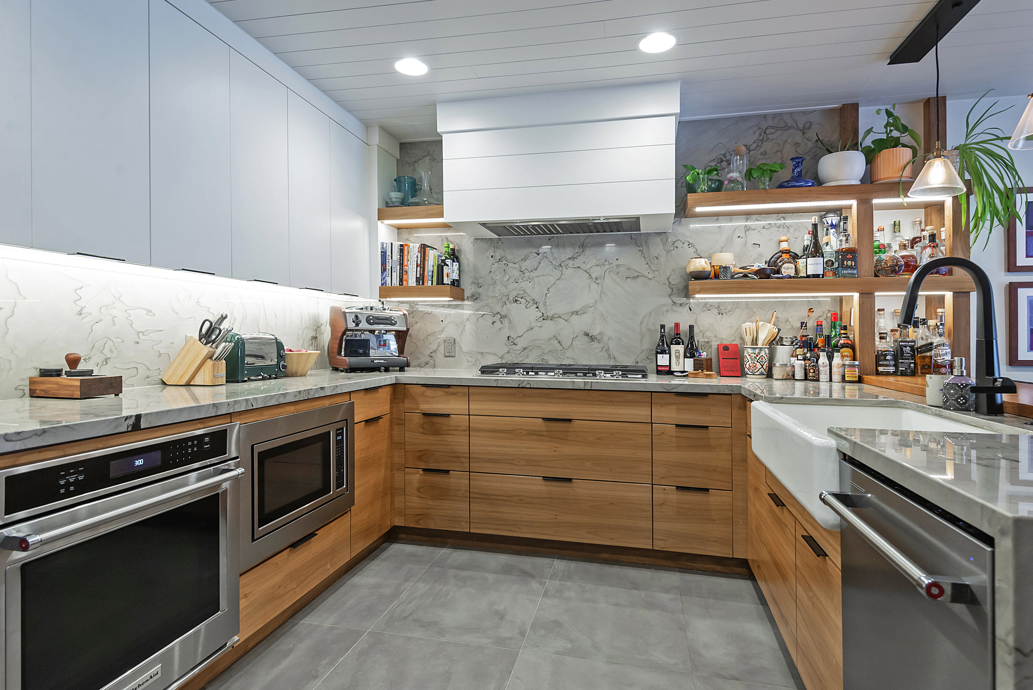Contemporary kitchen featuring wood-finish lower cabinetry, white upper cabinetry, and a full-height stone backsplash