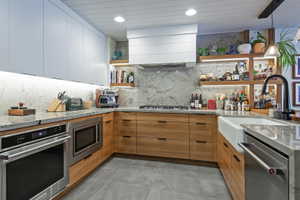 Contemporary kitchen featuring wood-finish lower cabinetry, white upper cabinetry, and a full-height stone backsplash