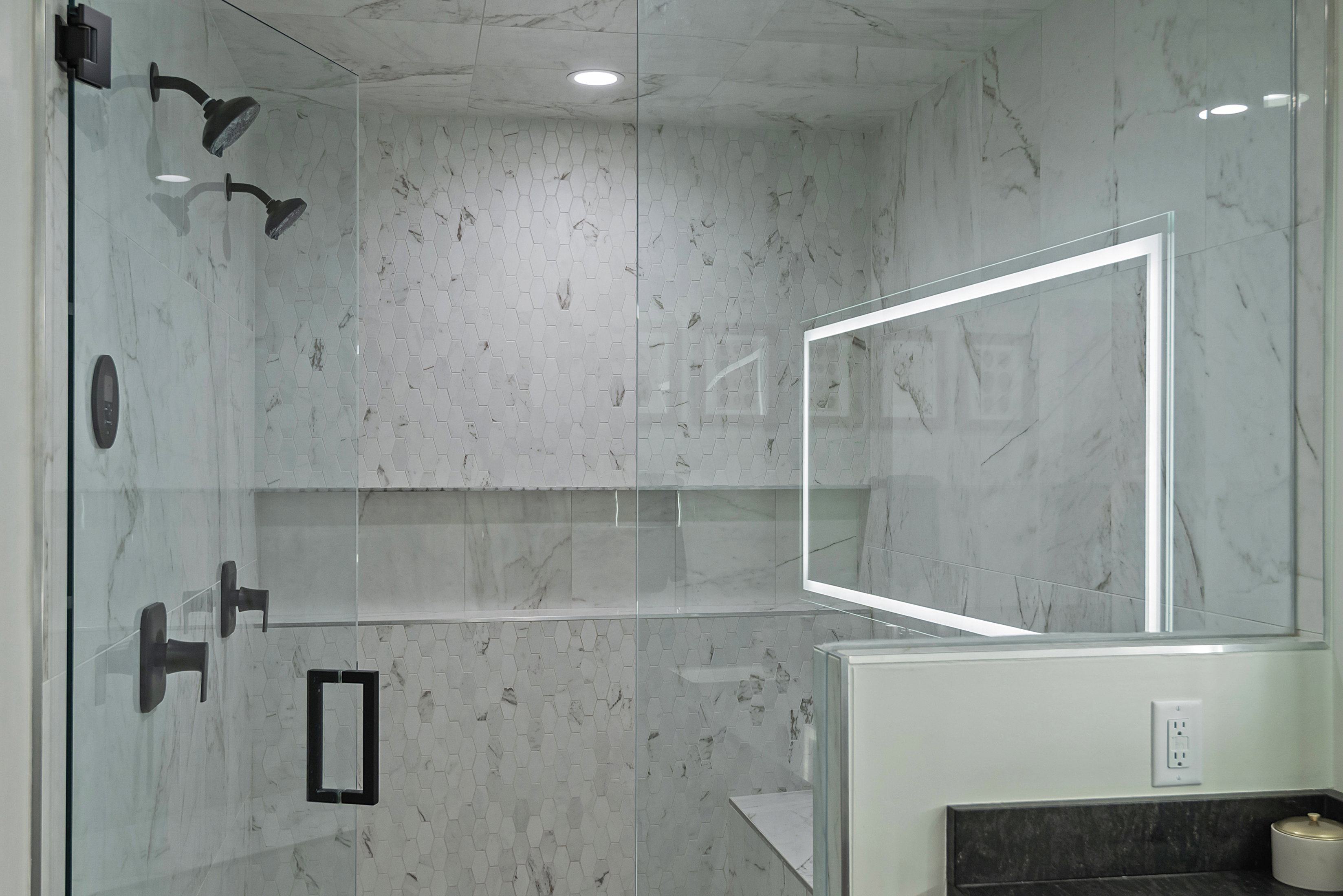 Glass-enclosed shower featuring dual matte black shower heads, white marble-look wall tiling, and a recessed product niche