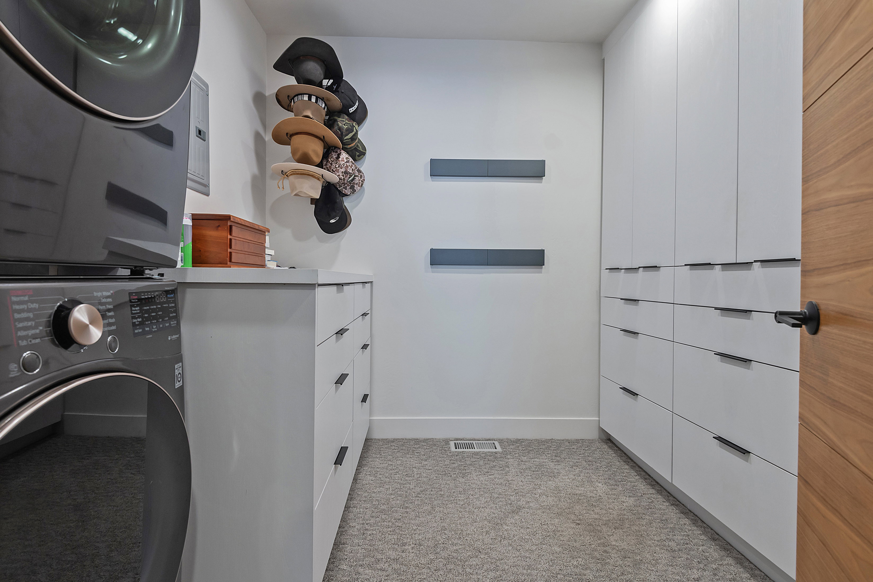 Laundry area featuring a stacked washer and dryer, integrated white cabinetry with dark hardware, a light gray countertop, and carpet flooring