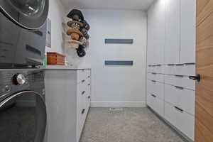 Laundry area featuring a stacked washer and dryer, integrated white cabinetry with dark hardware, a light gray countertop, and carpet flooring