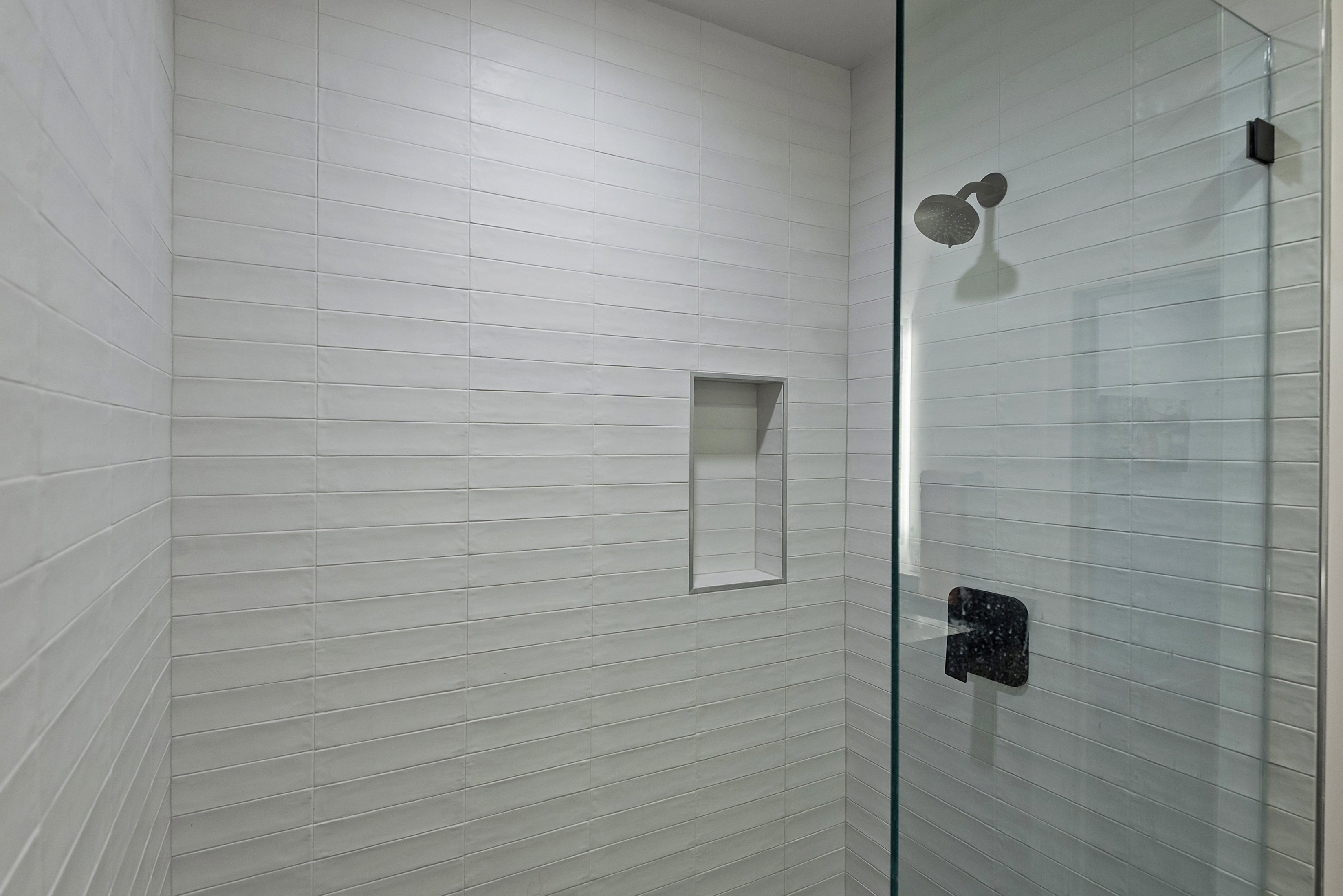 Glass-enclosed shower featuring horizontal white subway tile, an integrated shower niche, a dark bronze shower head, and a matching dark bronze shower handle