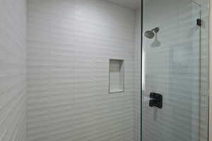 Glass-enclosed shower featuring horizontal white subway tile, an integrated shower niche, a dark bronze shower head, and a matching dark bronze shower handle