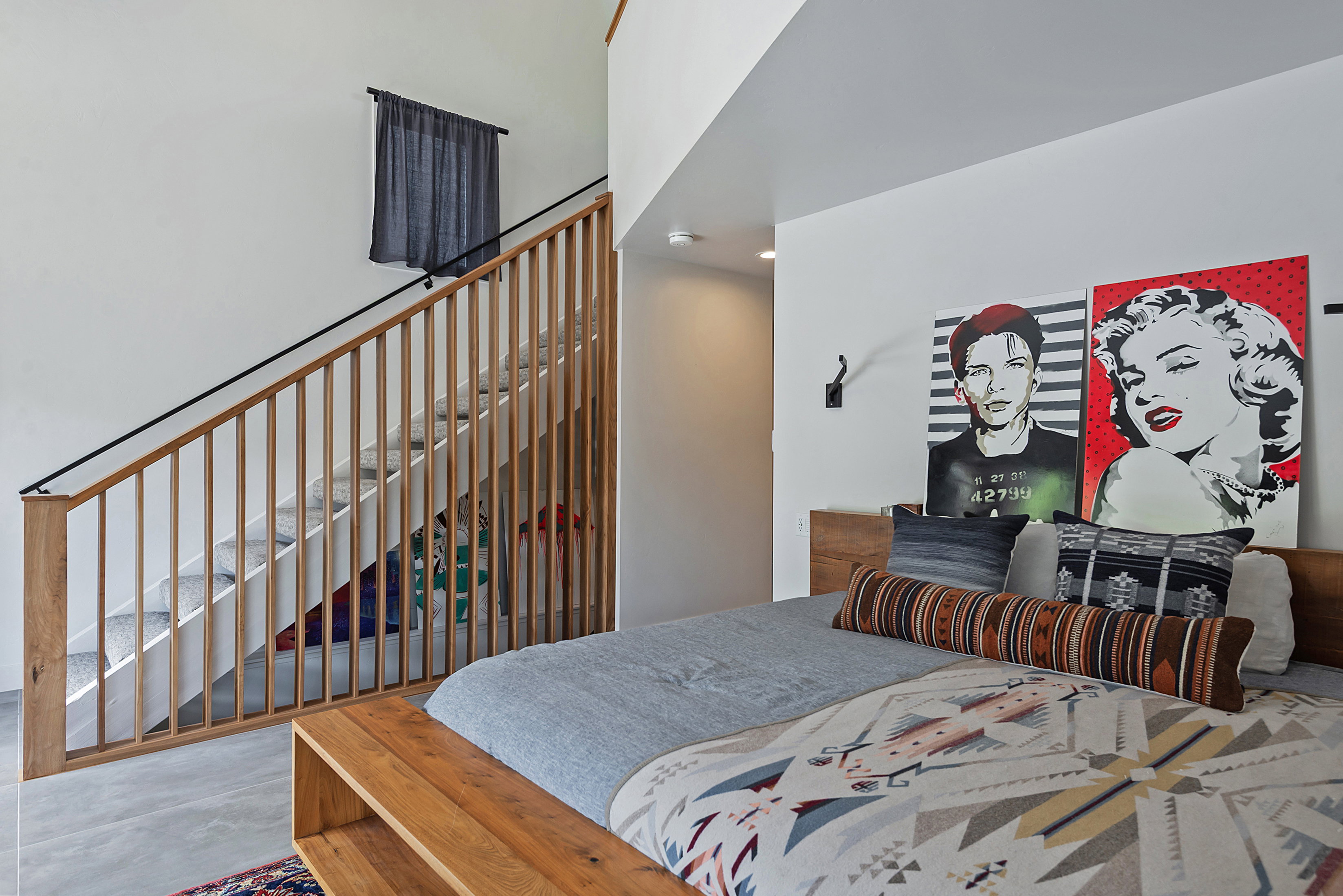 Bedroom featuring concrete flooring, a wood-finish bed frame, and a partial view of a staircase with wood-finish balusters and a black metal handrail