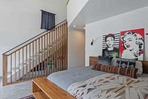 Bedroom featuring concrete flooring, a wood-finish bed frame, and a partial view of a staircase with wood-finish balusters and a black metal handrail