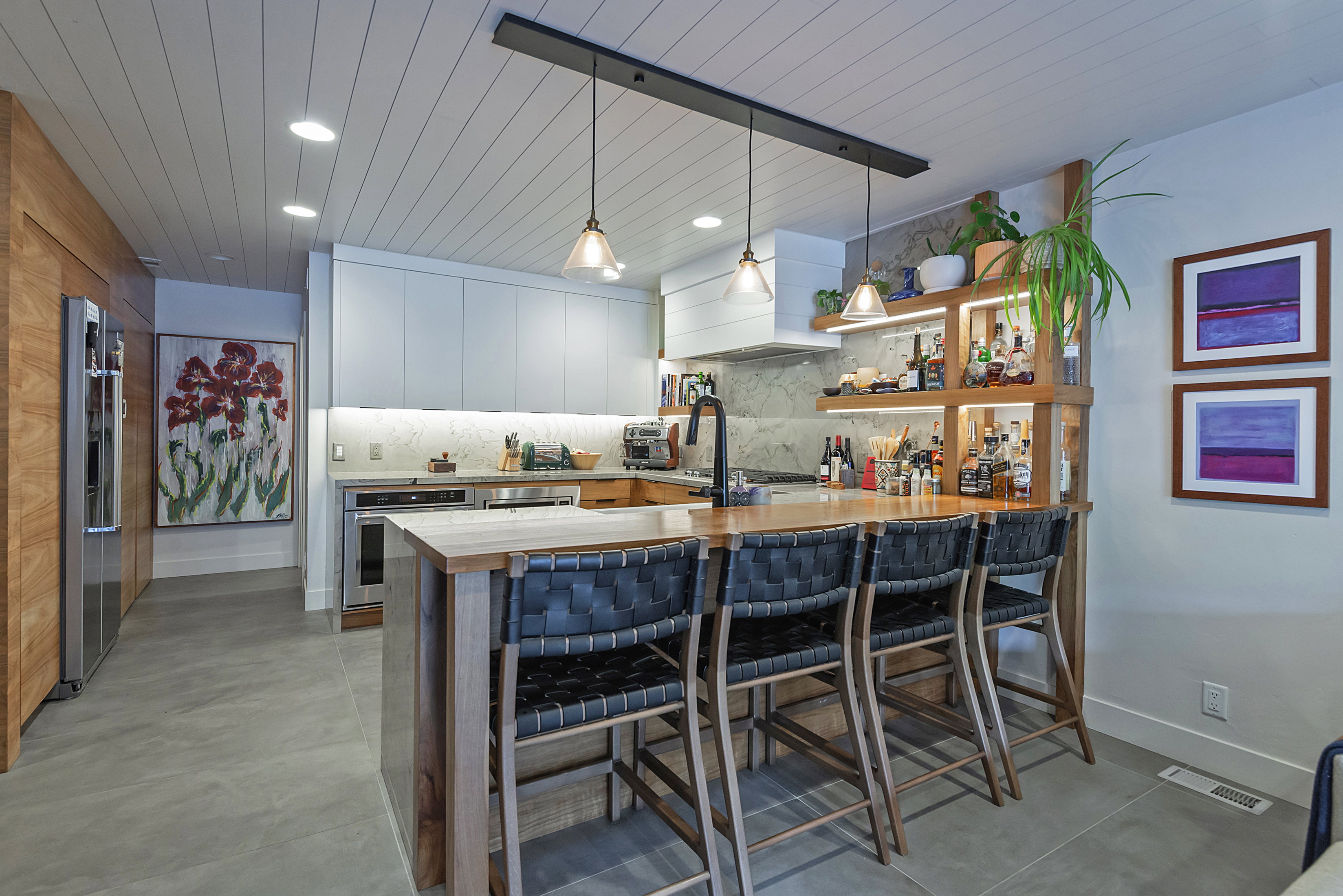 Spacious kitchen featuring a central island with bar seating, integrated shelving, under-cabinet lighting, panel-ready appliances, and a planked ceiling