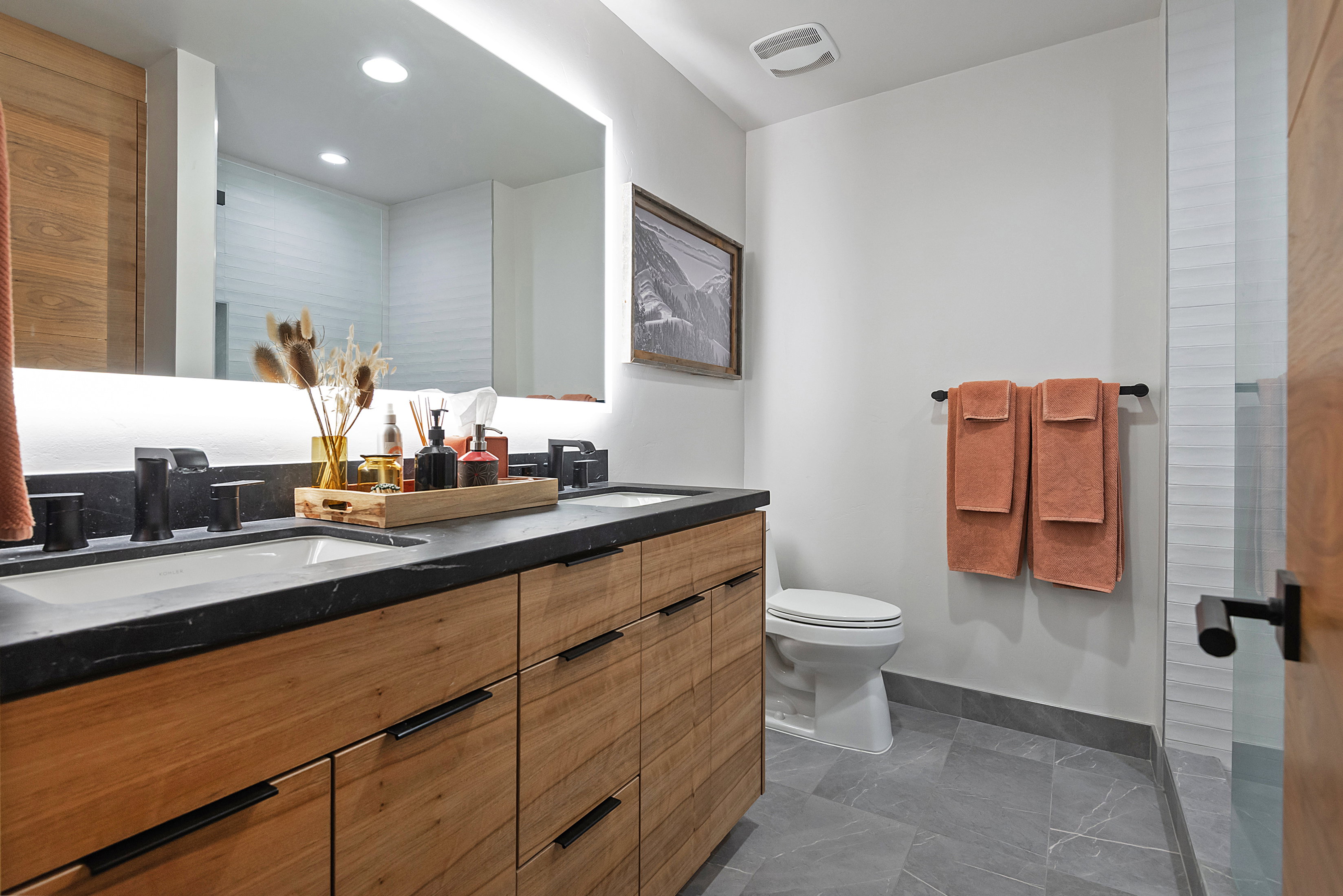 Modern bathroom featuring a dual vanity with wood-finish cabinetry and matte black hardware