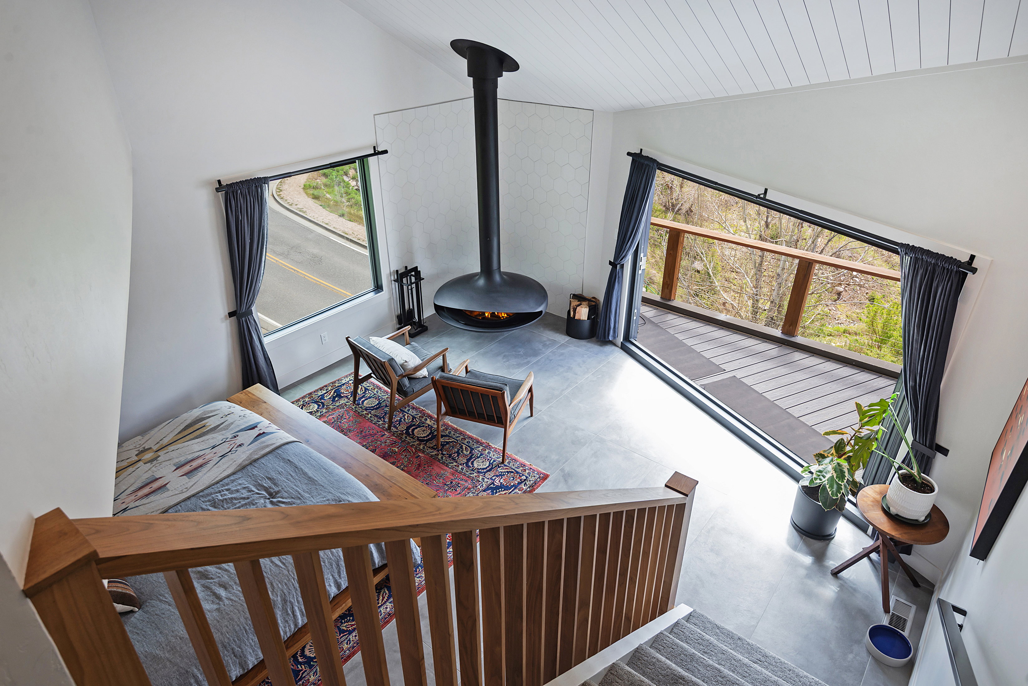 Loft space featuring a suspended fireplace, vaulted ceiling with wood-finish planks, large window, sliding glass door access to an outdoor deck with a wooden railing, and concrete flooring