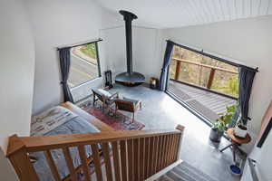 Loft space featuring a suspended fireplace, vaulted ceiling with wood-finish planks, large window, sliding glass door access to an outdoor deck with a wooden railing, and concrete flooring