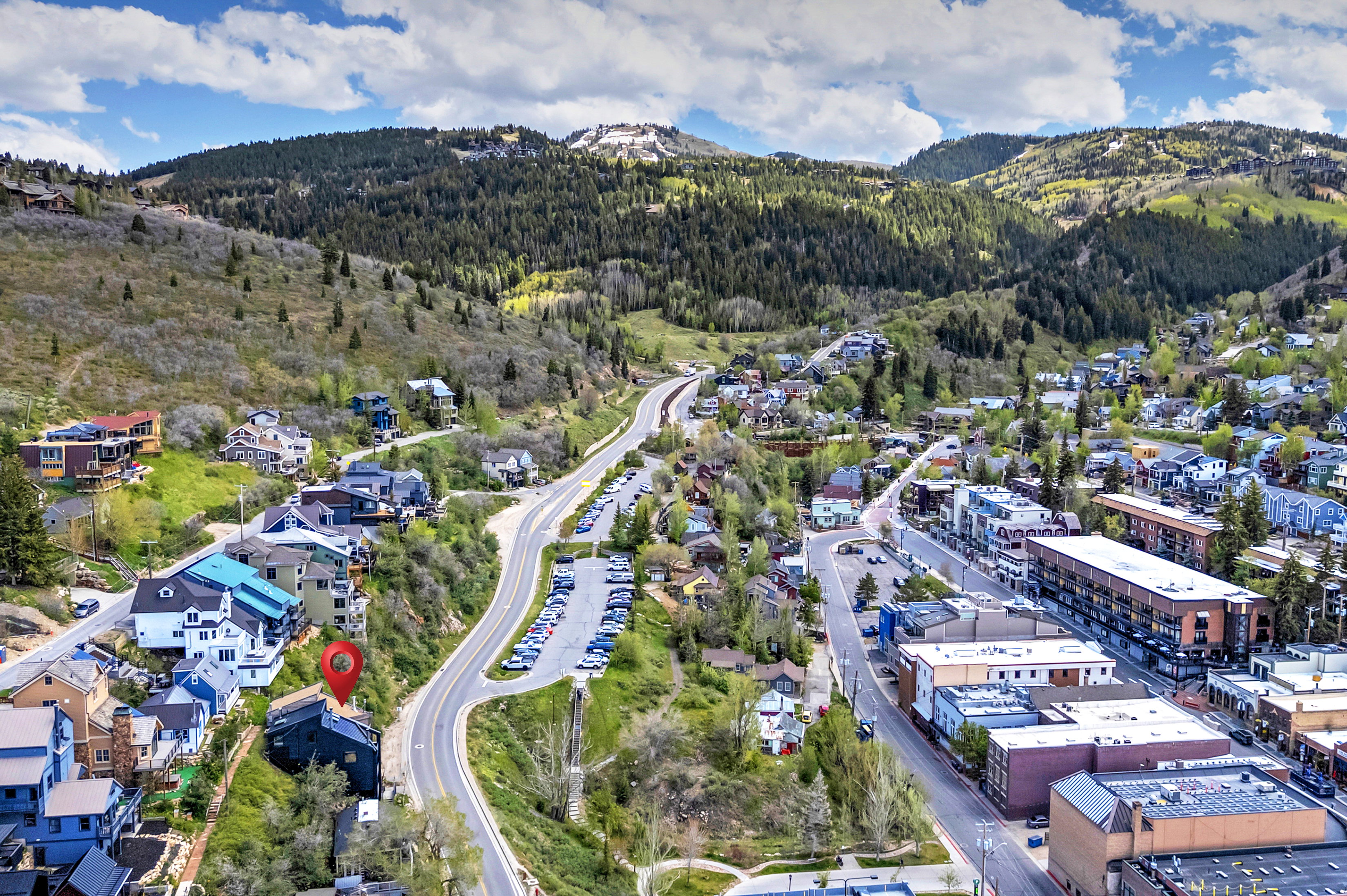Aerial perspective showcasing a residential structure situated on a sloping hillside, surrounded by mature trees and a mountainous backdrop