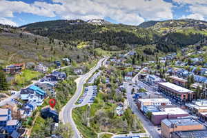 Aerial perspective showcasing a residential structure situated on a sloping hillside, surrounded by mature trees and a mountainous backdrop