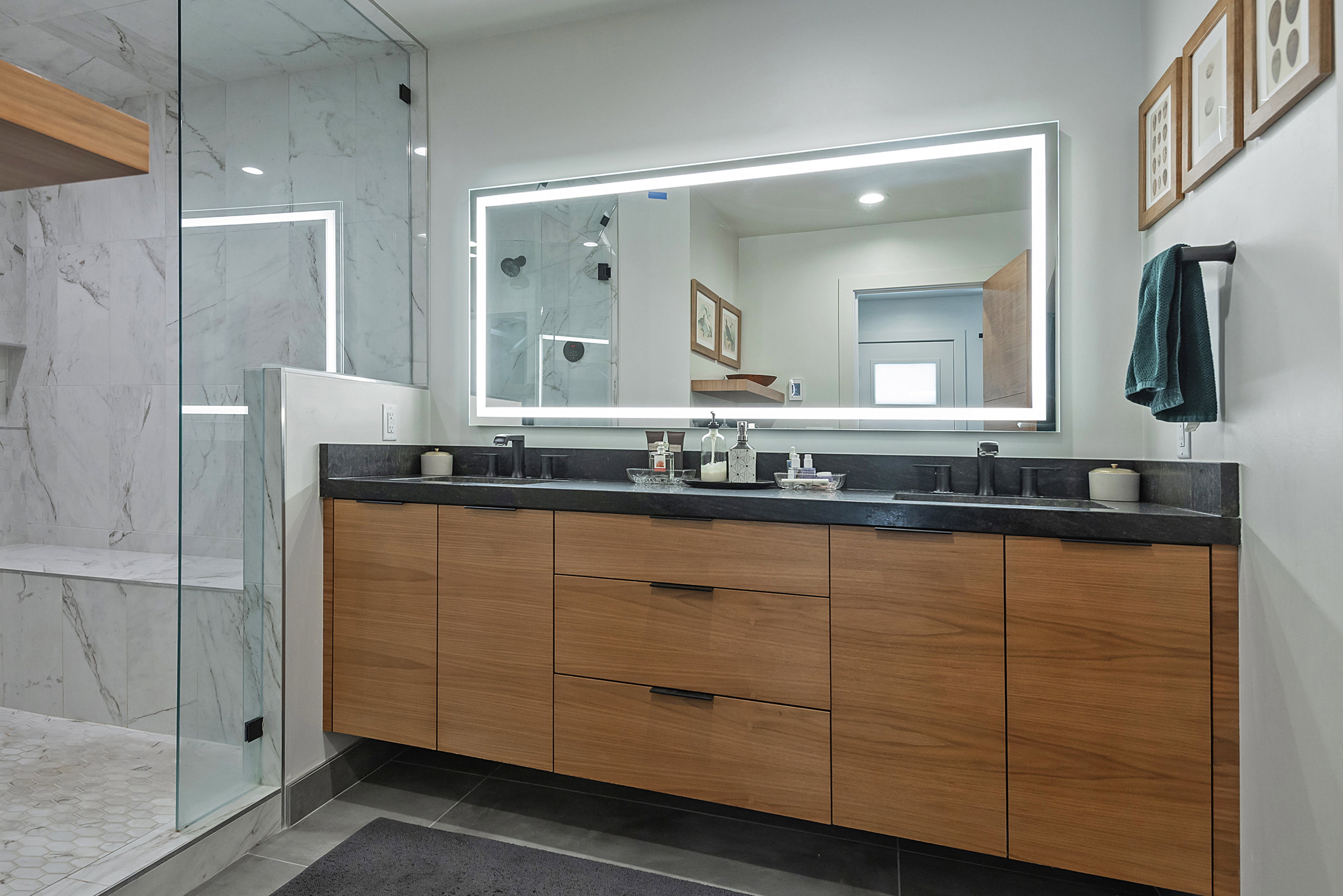 Modern bathroom featuring a floating wood-finish vanity with dual sinks and dark countertops