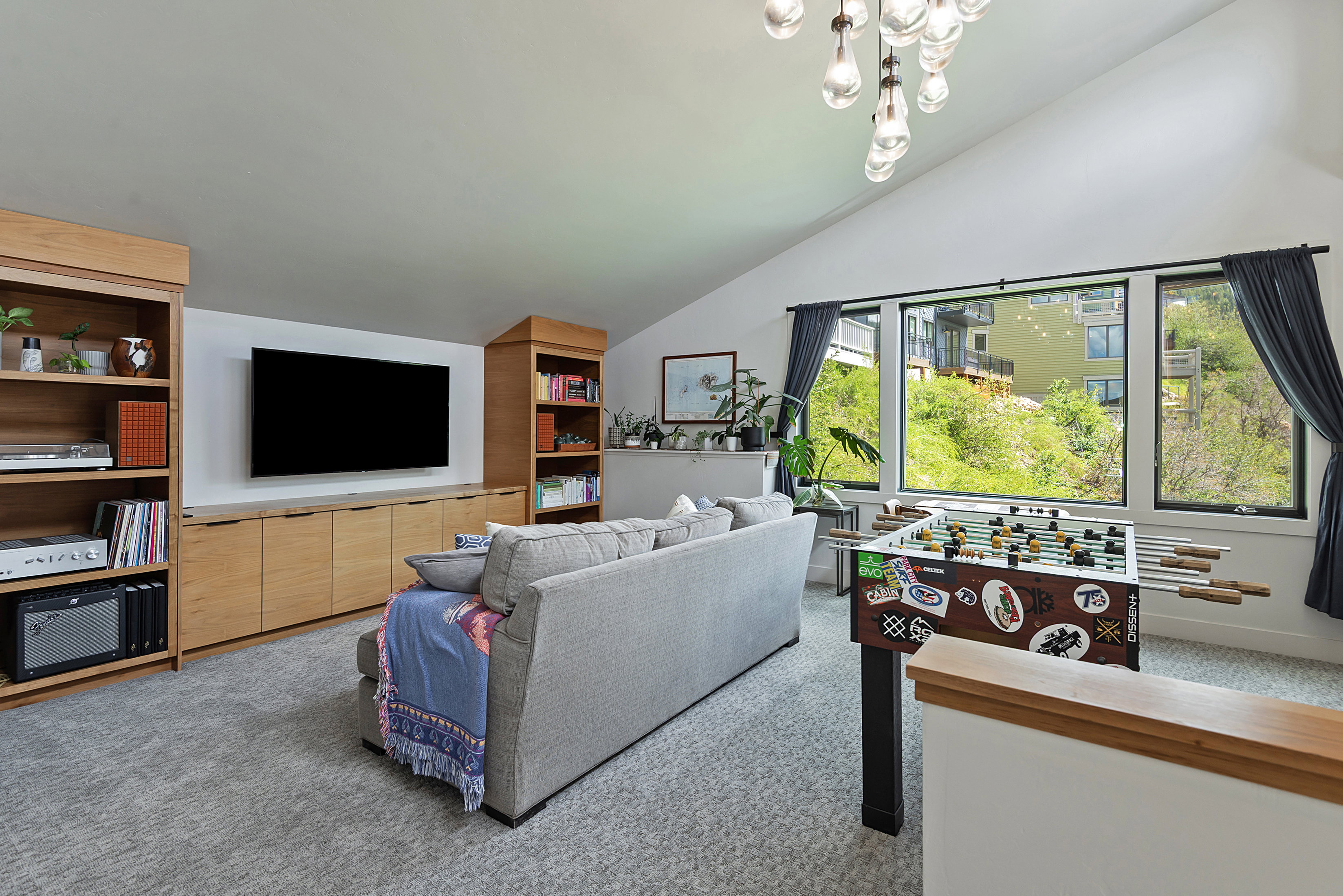 Vaulted ceiling room featuring light-toned built-in shelving and cabinetry, a large picture window, and gray carpet flooring