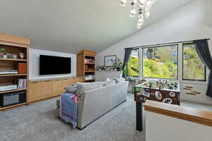 Vaulted ceiling room featuring light-toned built-in shelving and cabinetry, a large picture window, and gray carpet flooring