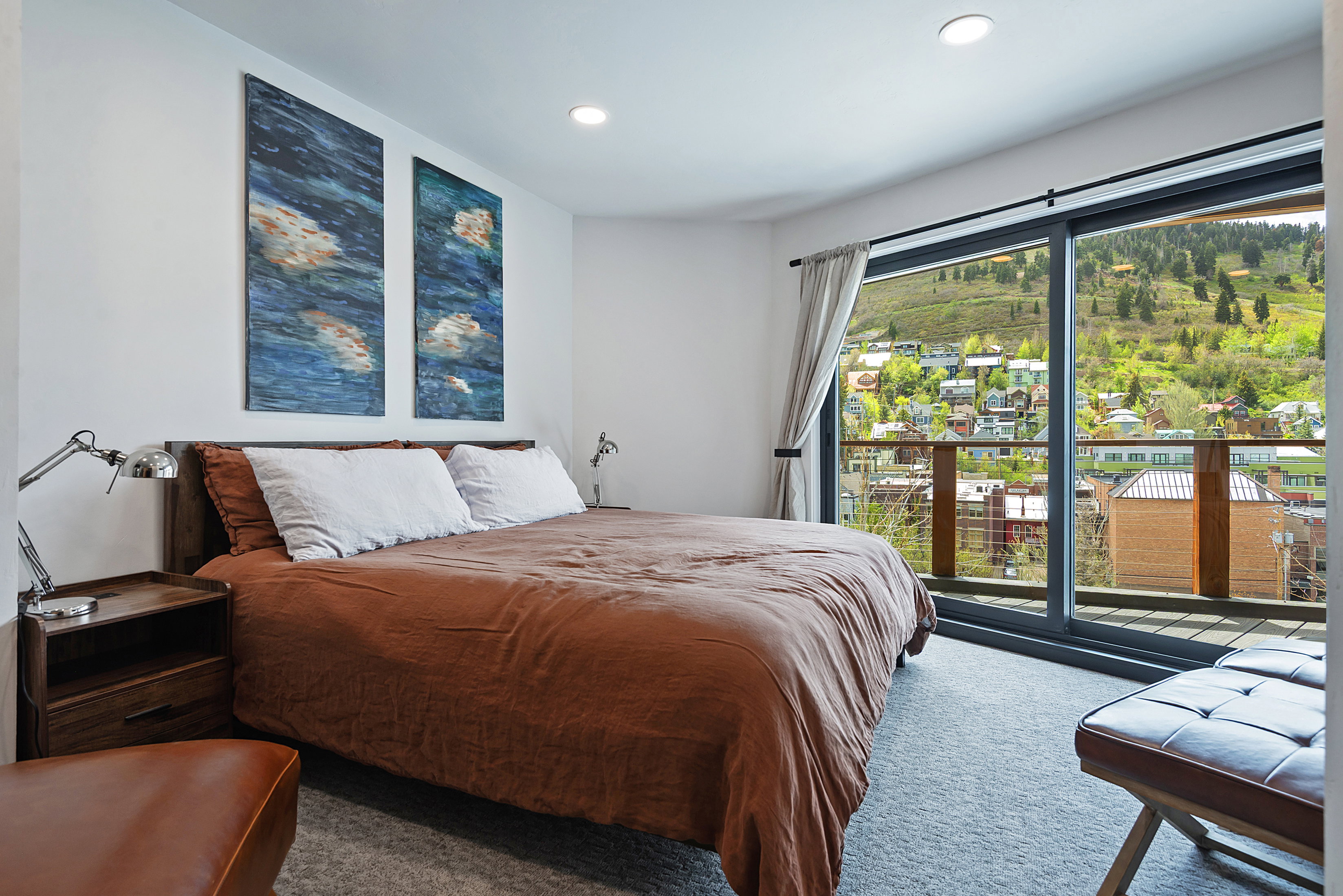 Sliding glass door opening to an outdoor balcony with metal and wood railing, providing a mountain and townscape backdrop