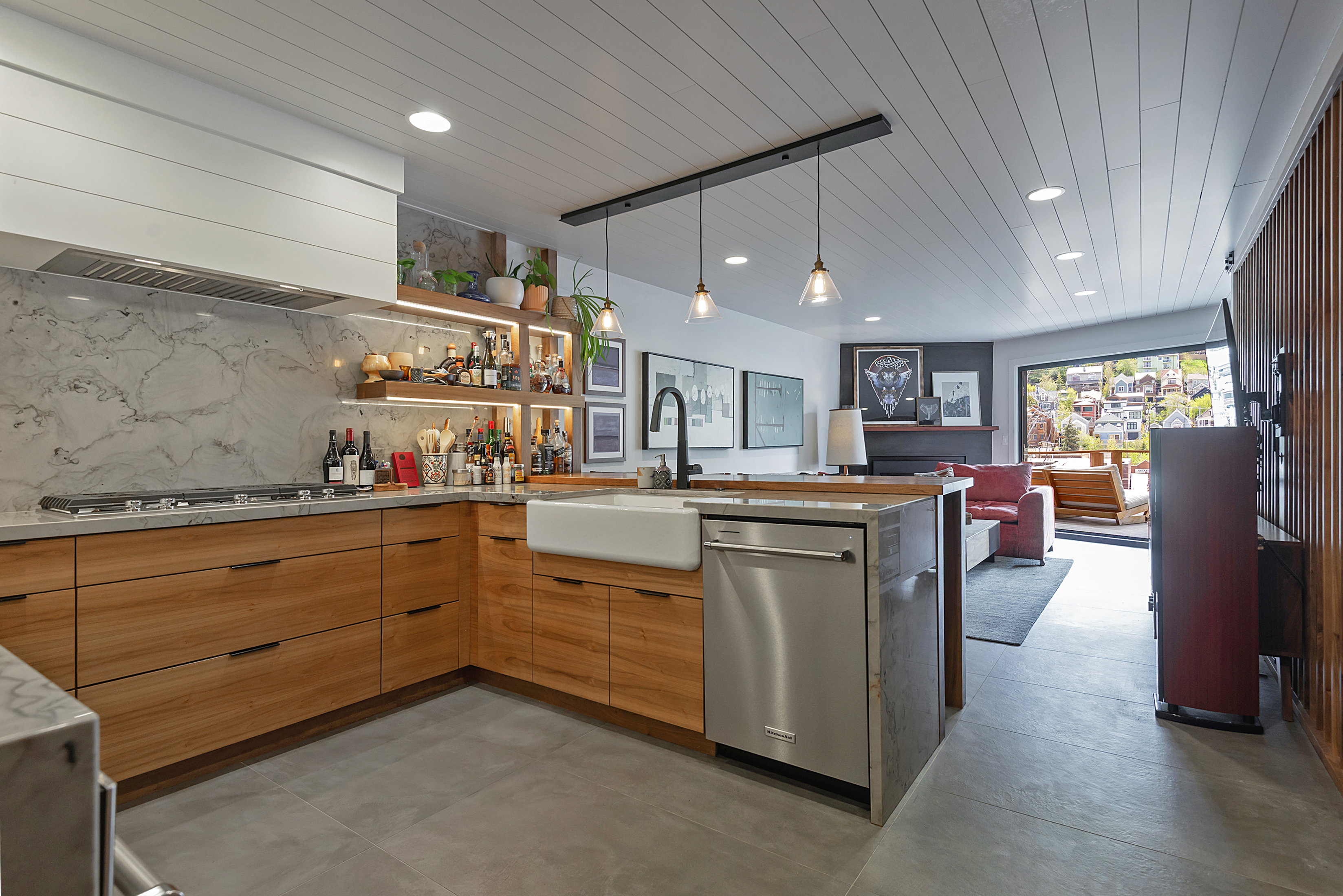Open-concept kitchen featuring wood cabinetry, stone countertops, a farmhouse sink, stainless steel appliances, and a marble backsplash