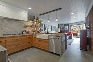Open-concept kitchen featuring wood cabinetry, stone countertops, a farmhouse sink, stainless steel appliances, and a marble backsplash