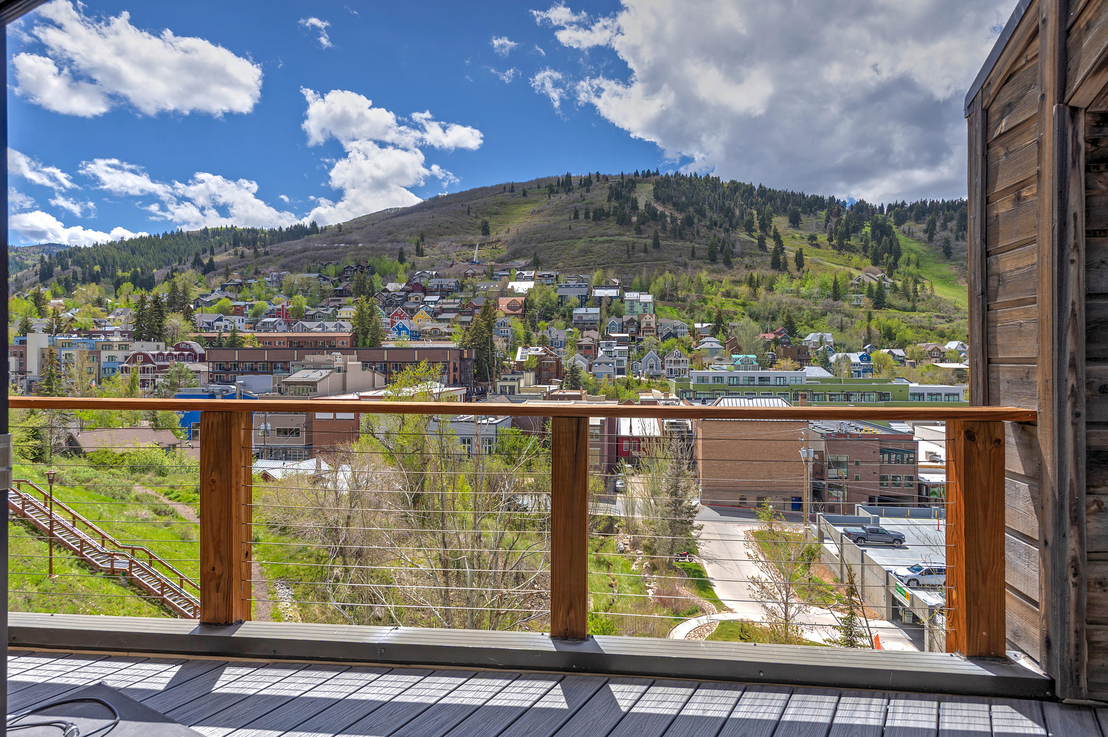 Deck with composite flooring and wood railing featuring cable infill, overlooking a mountain landscape with distant structures
