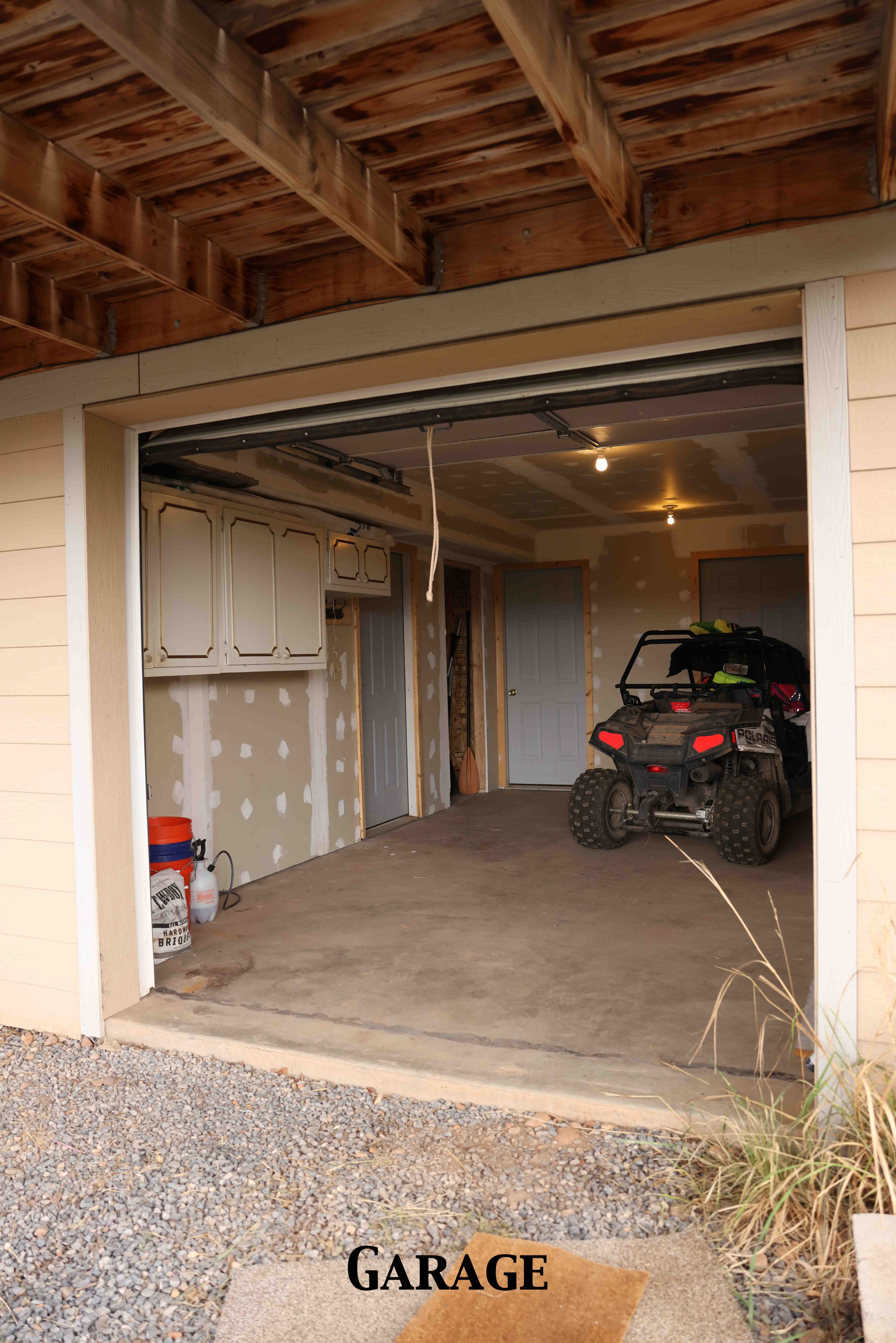 Unfinished garage space featuring a concrete floor, exposed ceiling joists, and built-in white cabinetry