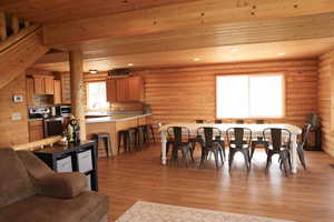 Open-concept living space featuring log walls, wood-finish flooring, and a dining area with a large table