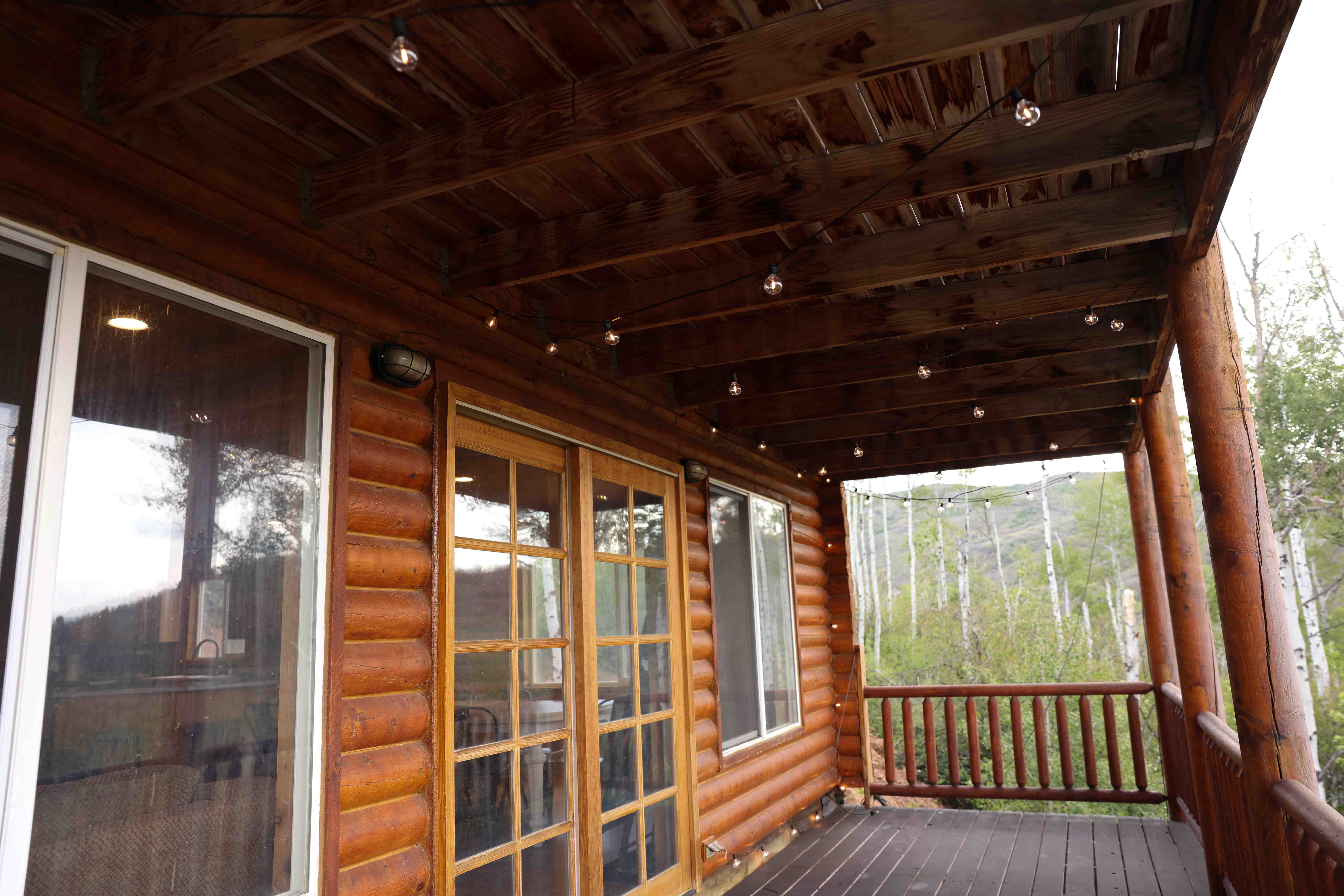 Expansive wooden deck featuring log column supports, a wooden railing, and string lighting