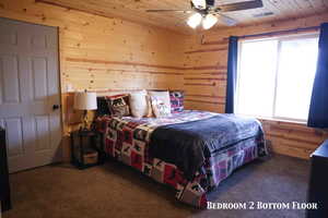 Pine wood paneling and ceiling throughout, featuring a ceiling fan with integrated lighting, a large window with privacy curtains, and soft carpet flooring