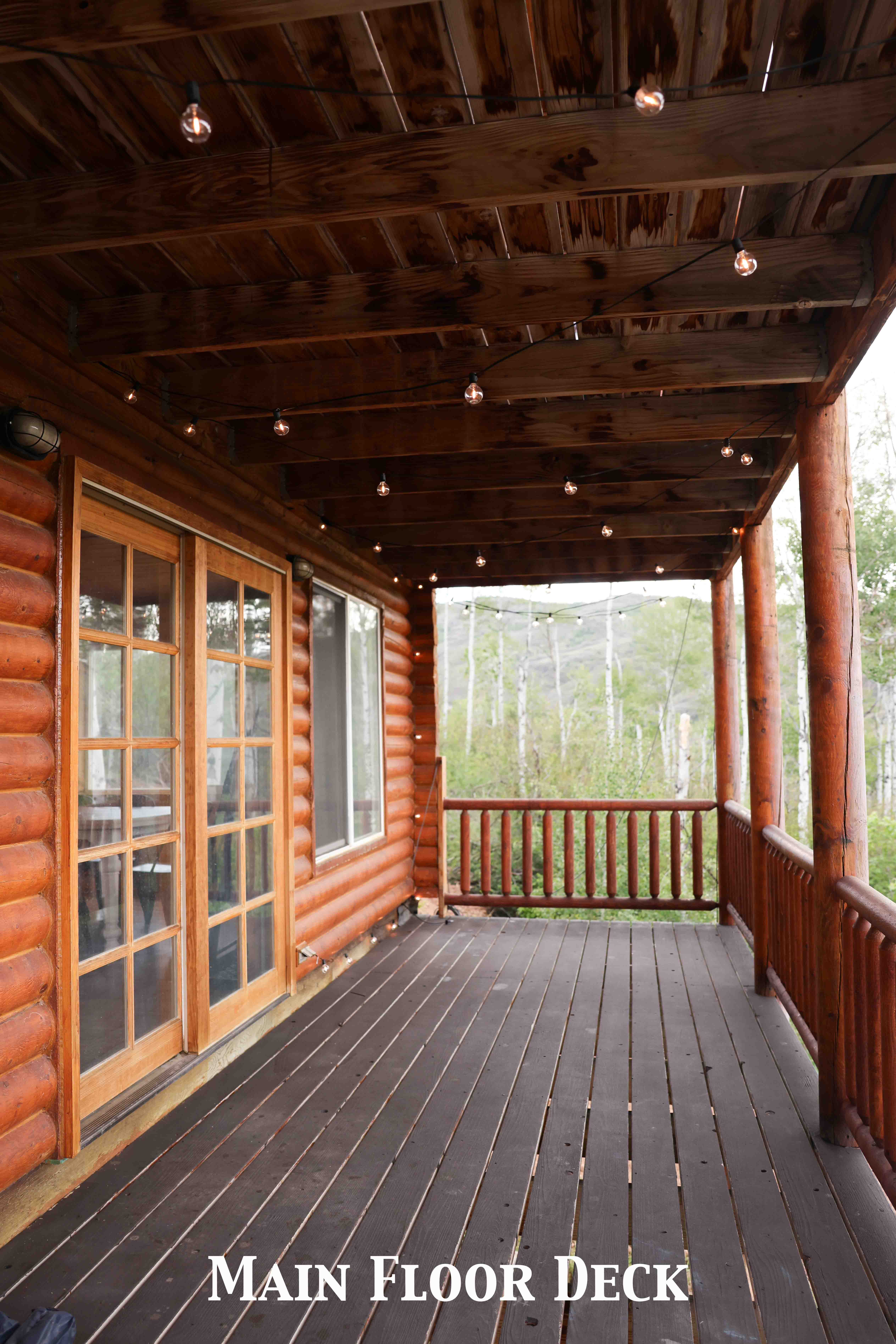 Covered outdoor deck with dark wood-finish flooring, log siding exterior, and wood-framed French doors