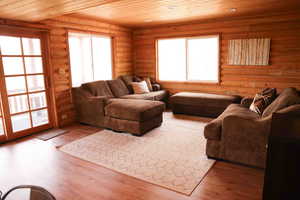 Living area featuring log walls, wood-finish flooring, a wood-paneled ceiling, and a glass sliding door opening to an outdoor area