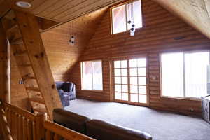 Spacious room featuring log wall construction, vaulted wood-paneled ceiling, and light gray carpeting
