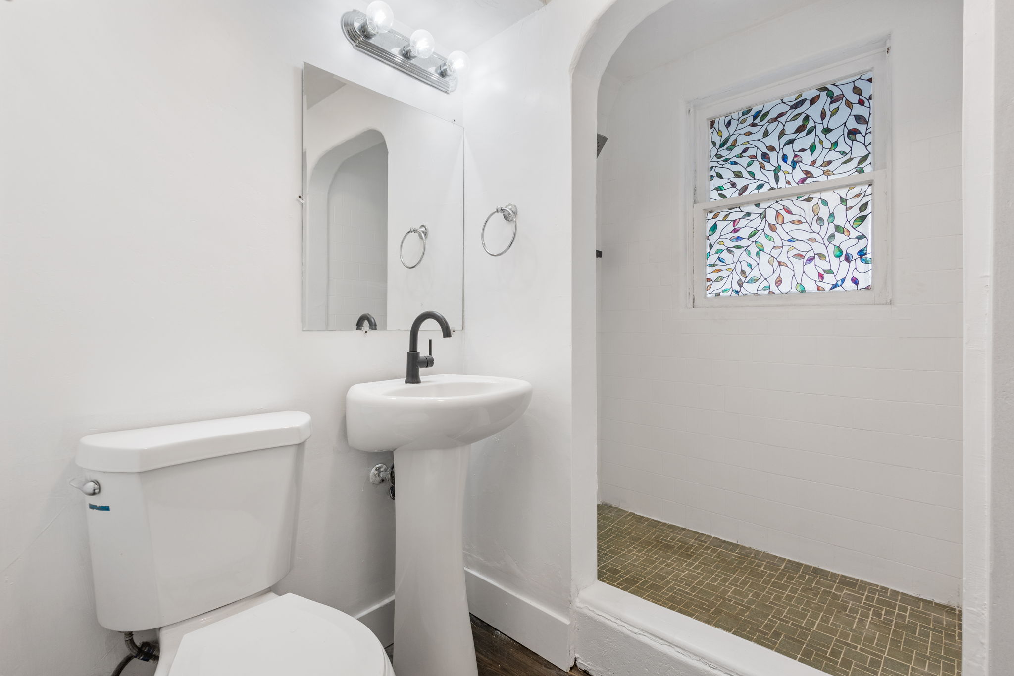Bathroom featuring a pedestal sink with a matte black faucet, a wall-mounted mirror, and overhead vanity lighting