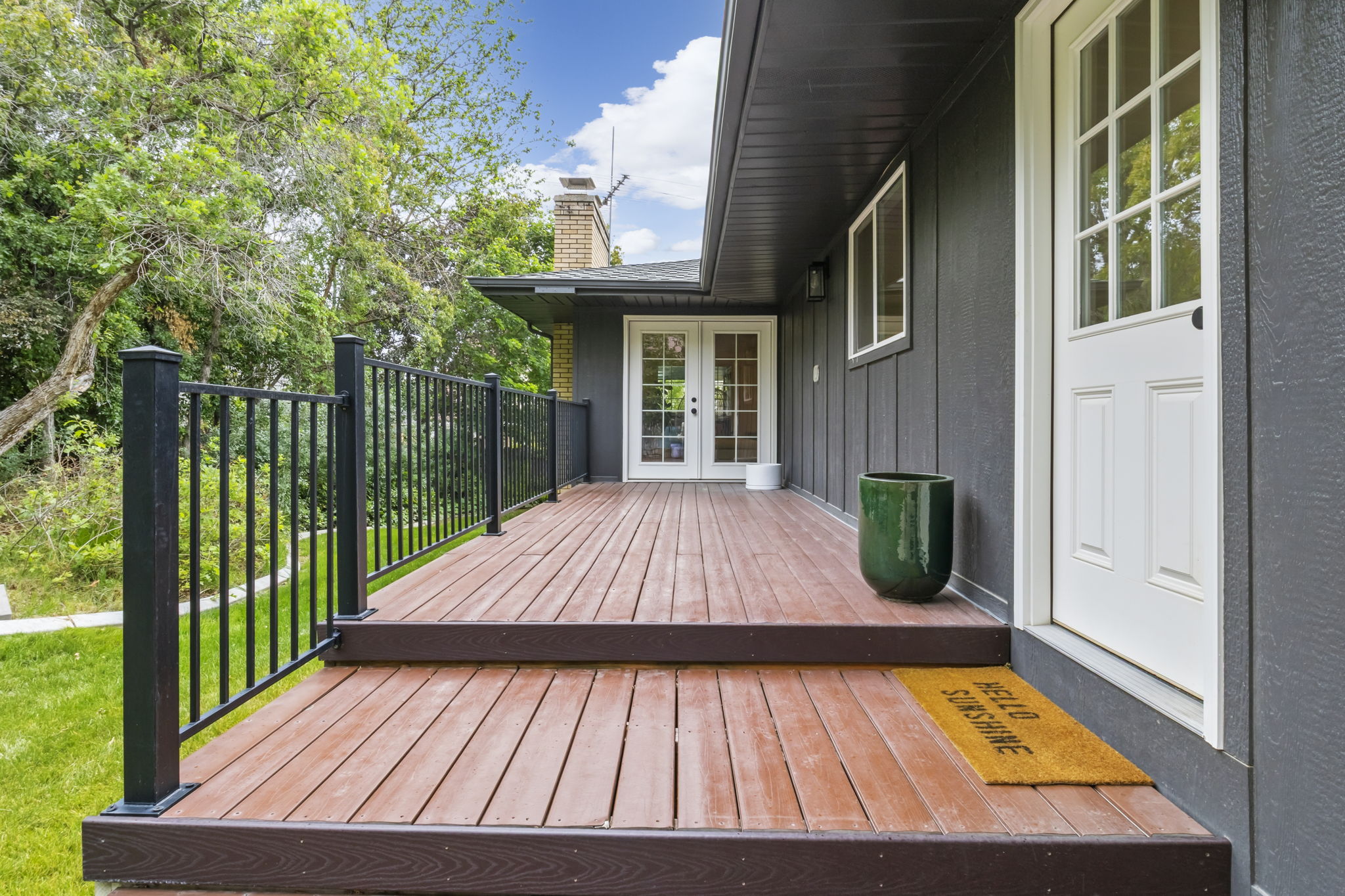 Expansive wood-finish deck with black metal railing, featuring a white paneled door with glass inserts and an additional set of white French doors