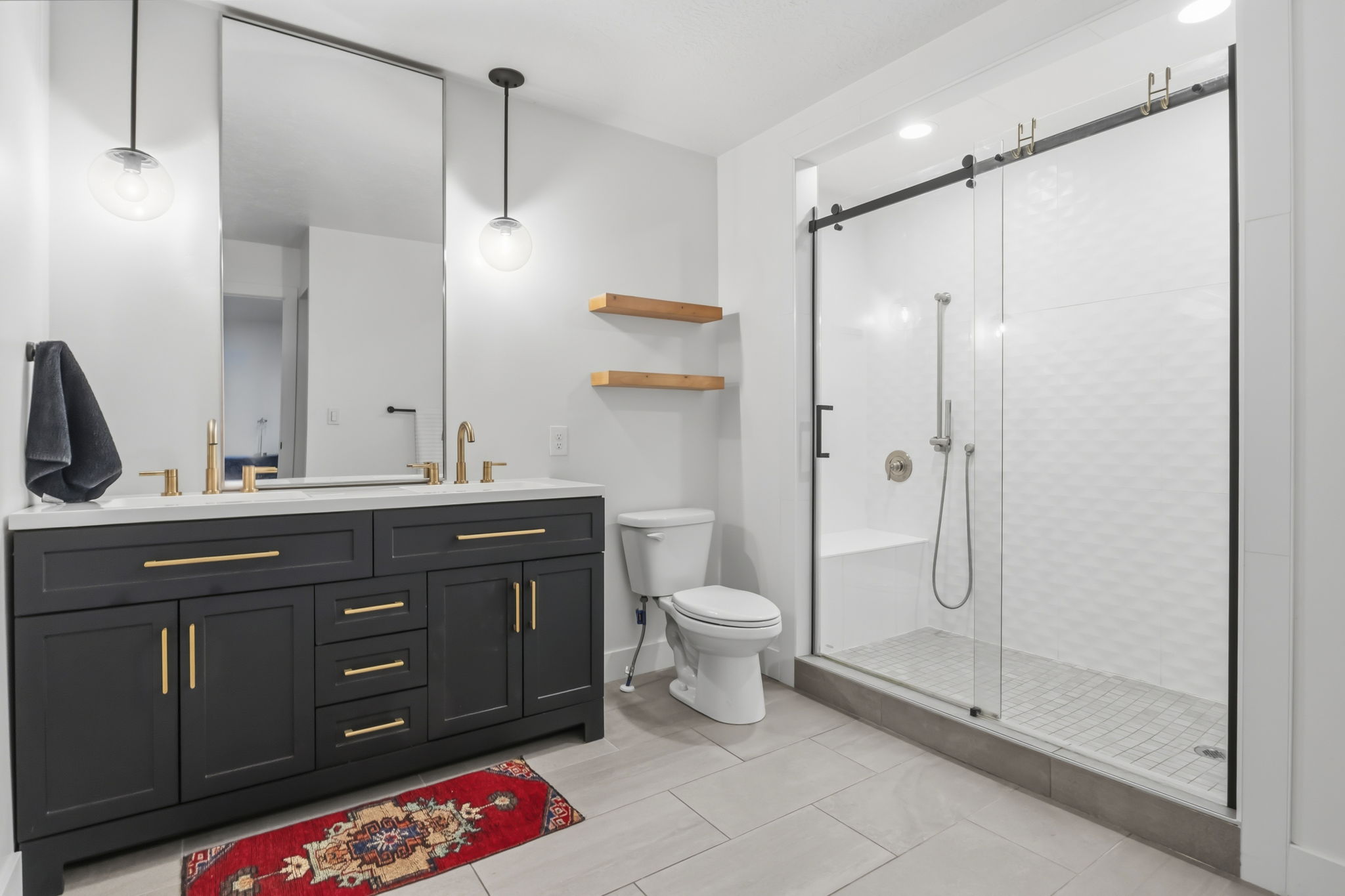 Modern bathroom featuring a double vanity with dark cabinetry, gold-finish hardware, and a light-toned countertop