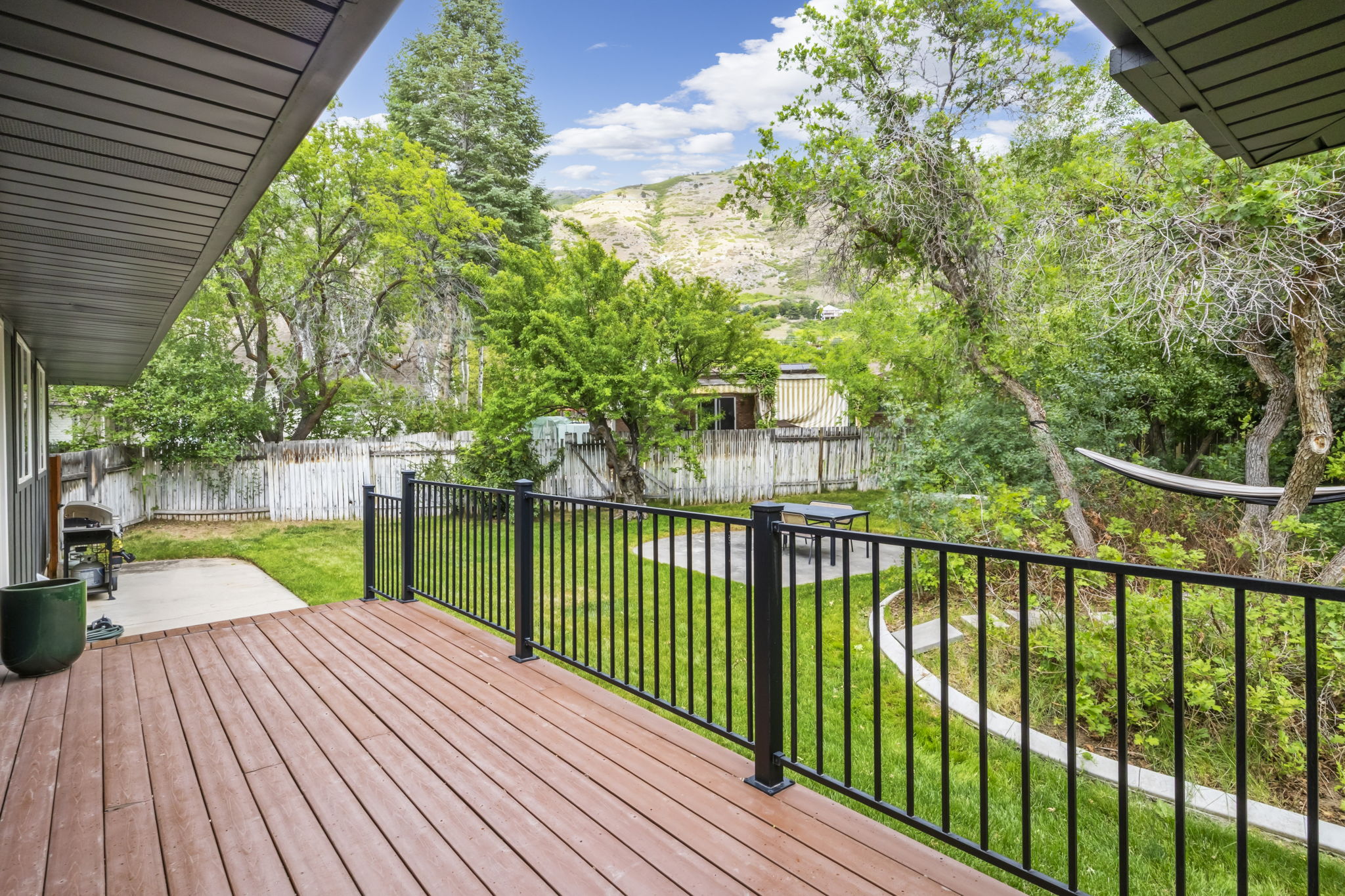 Expansive wood-finish deck with black metal railings, overlooking a verdant backyard with mature trees and a fenced perimeter