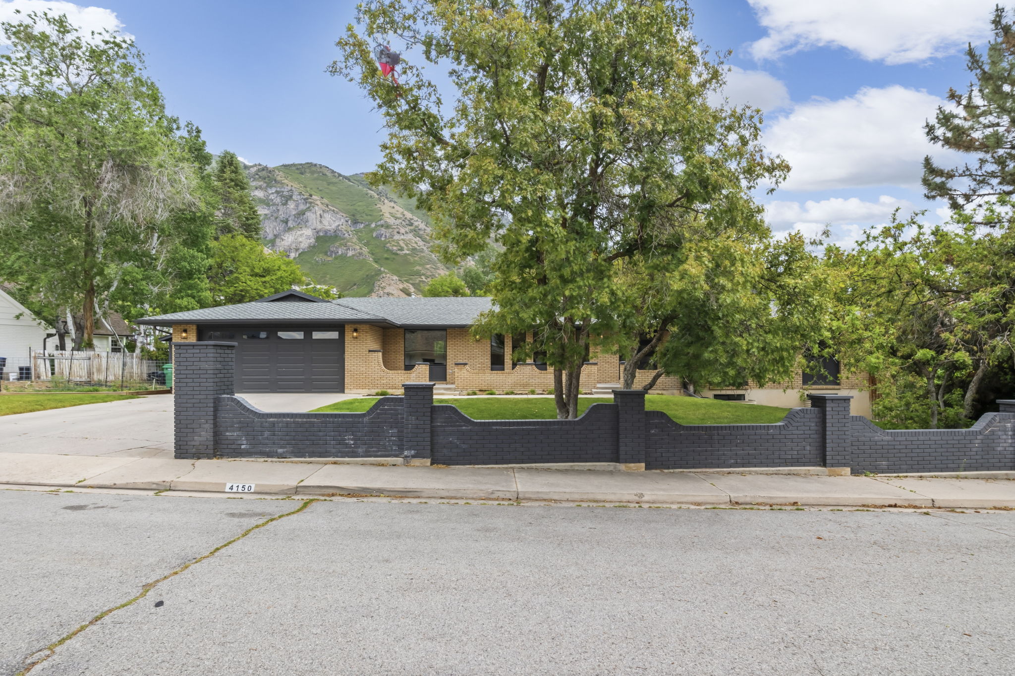 Ranch-style residence featuring a distinctive dark brick privacy wall and an attached garage with a dark panel door