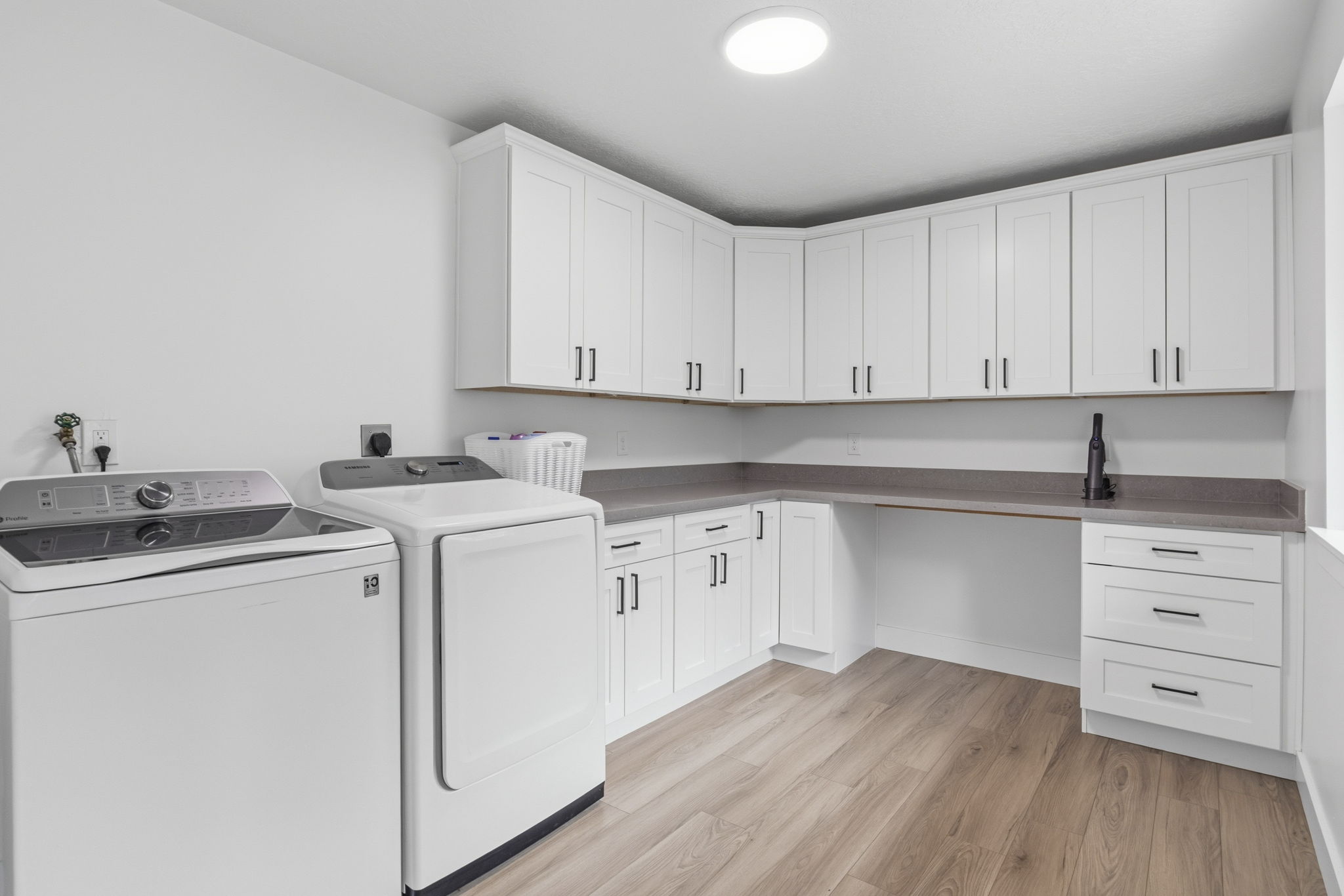 Dedicated laundry space featuring extensive white cabinetry, durable countertops, wood-finish flooring, and a circular ceiling light fixture