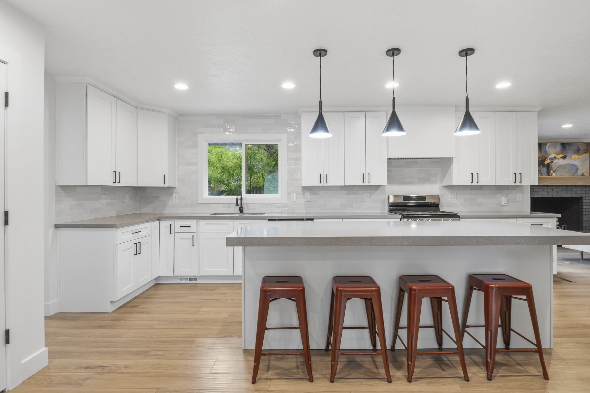 Modern kitchen featuring an expansive island with a light-toned countertop, white shaker-style cabinetry, and wood-finish flooring