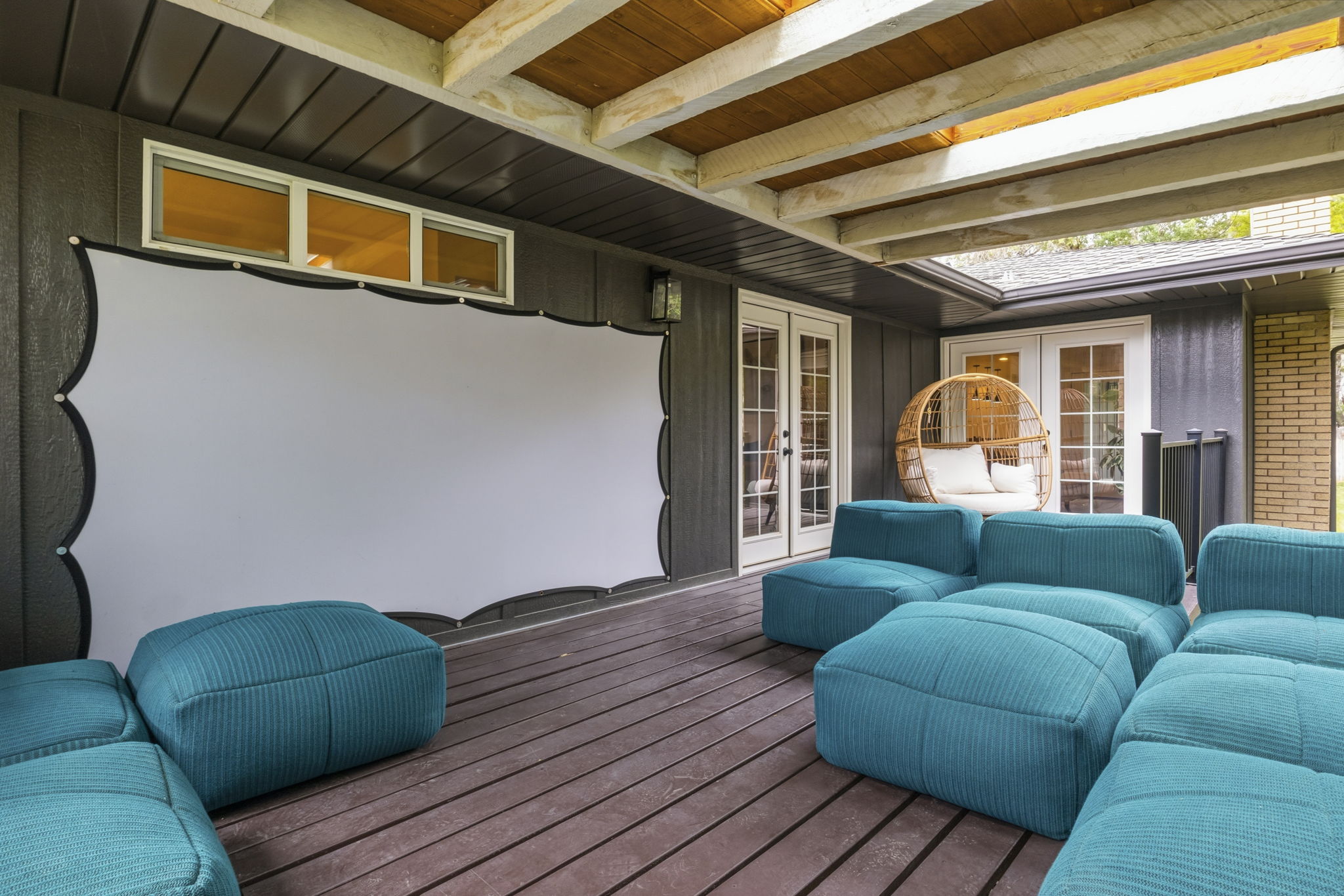 Covered outdoor patio featuring a large projection screen, two sets of French doors, wood-finish decking, and an exposed beam ceiling