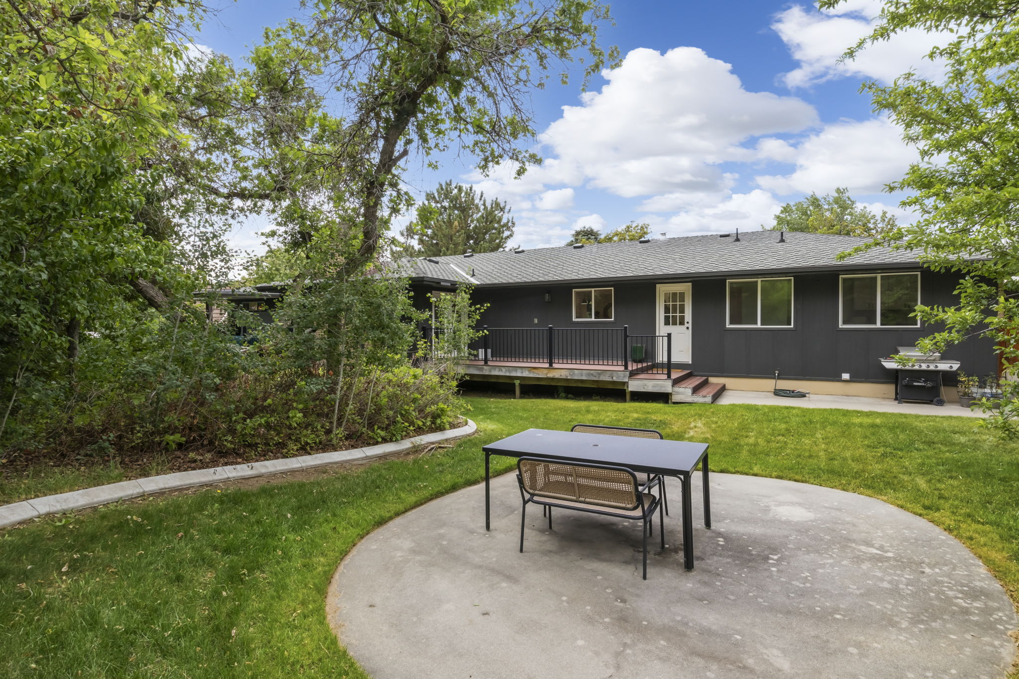 Spacious backyard featuring a large concrete patio, expansive lawn, and mature trees