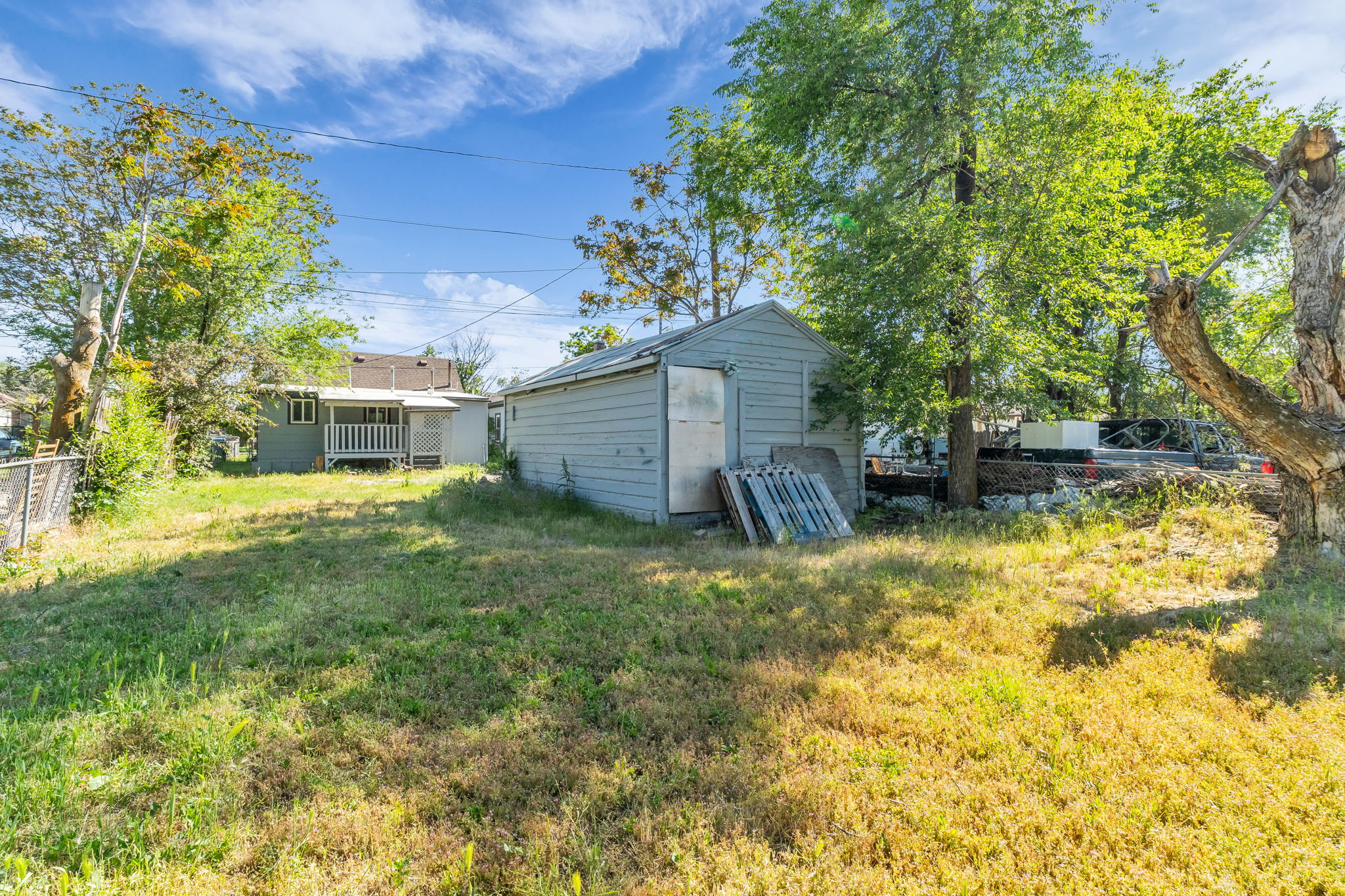 Backyard featuring a shed with horizontal siding, mature trees, and a distant property with a covered porch