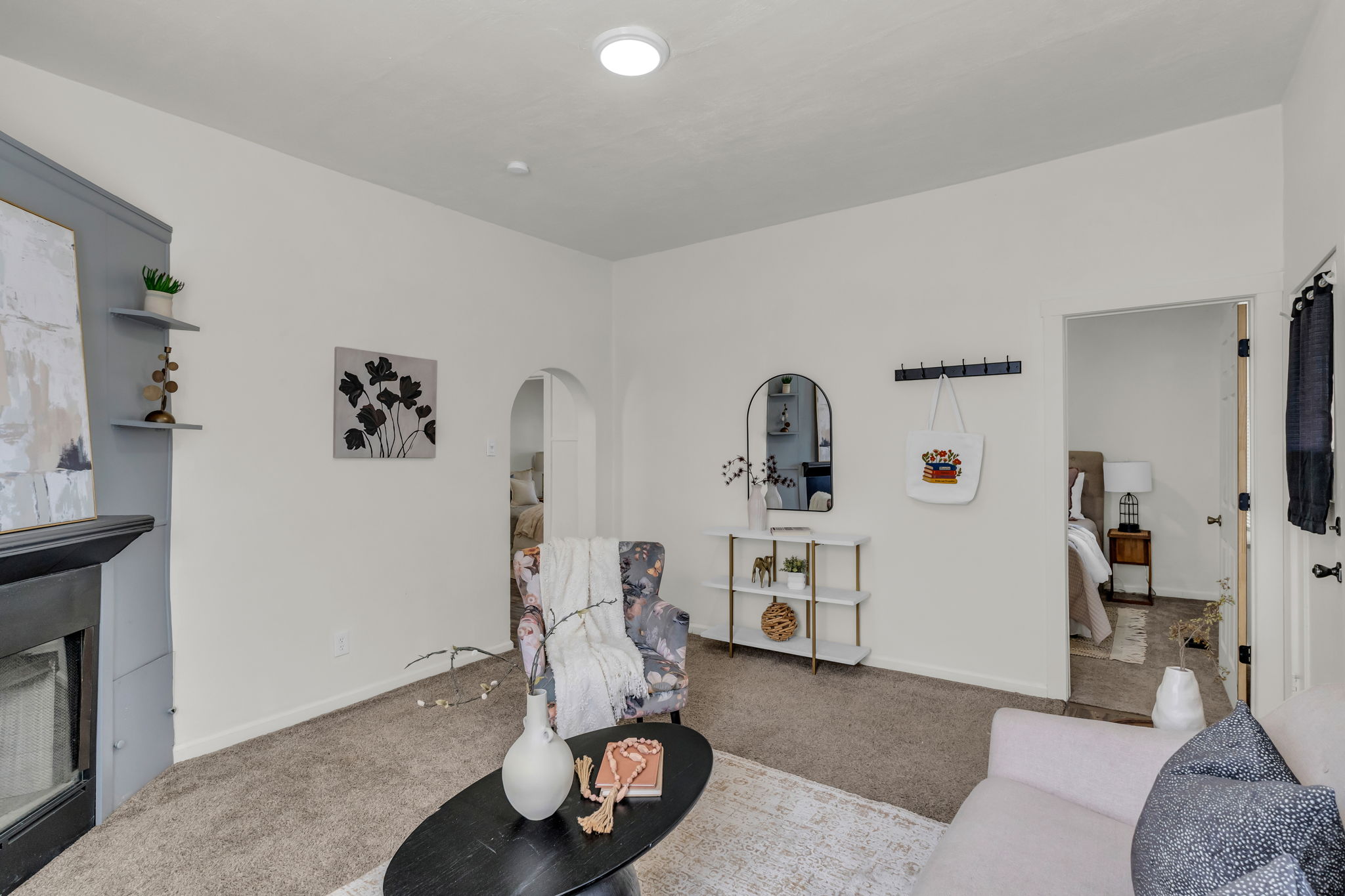 Carpeted living area featuring a fireplace with built-in shelving, an arched doorway, and an open doorway to an additional room