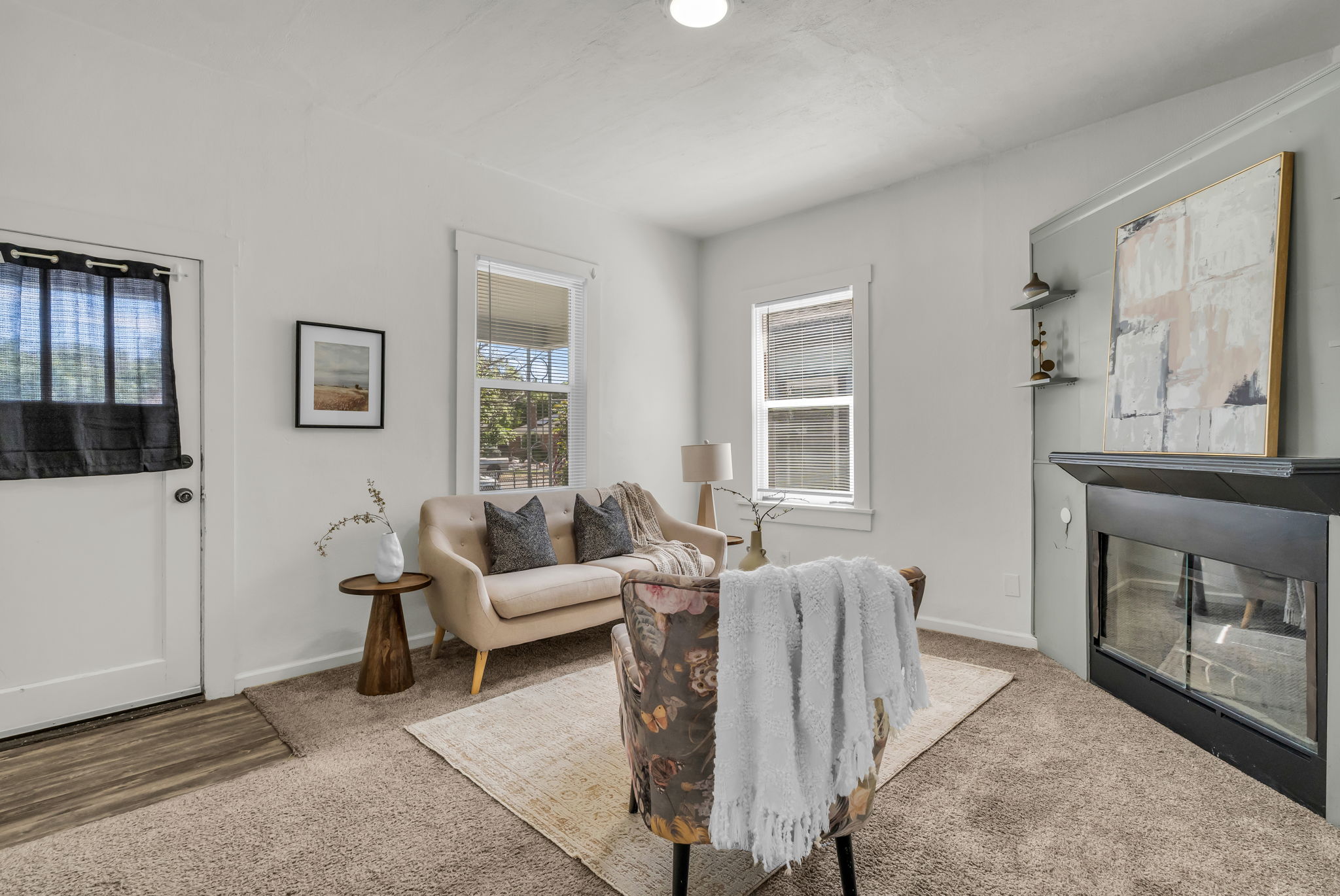 Living area featuring a fireplace with a black mantel, two windows with white trim, and light-colored carpeting