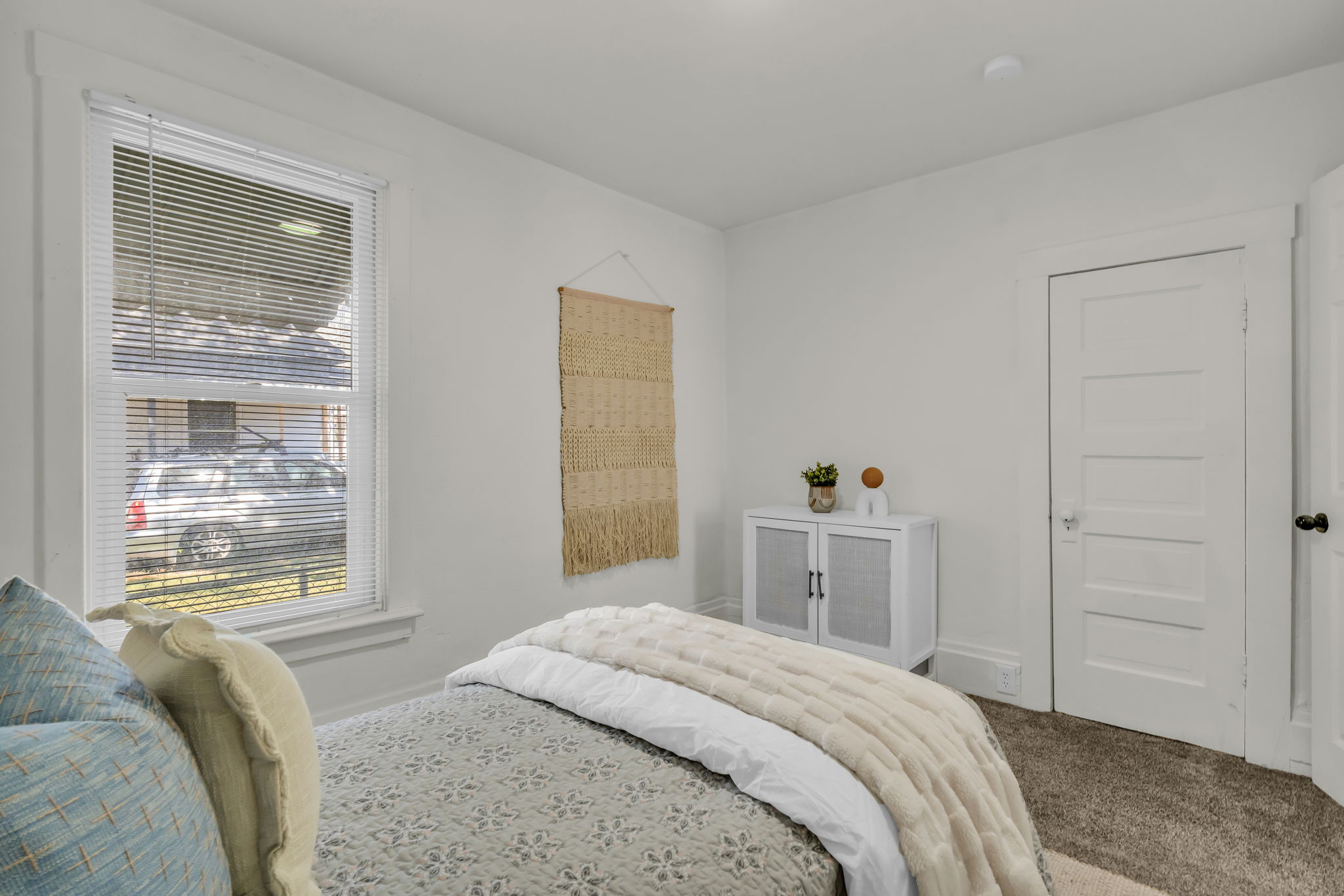 Light-filled room featuring white walls, carpeted flooring, a multi-pane window with blinds, and white trim