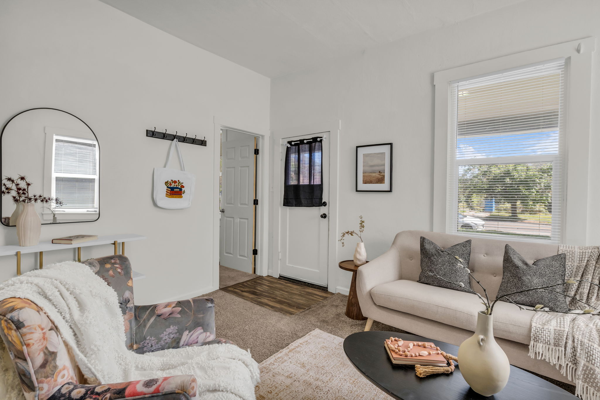 Living space featuring neutral wall tones, carpeted flooring, a white trim window, a white paneled interior door, and a partially visible wood-finish flooring entryway