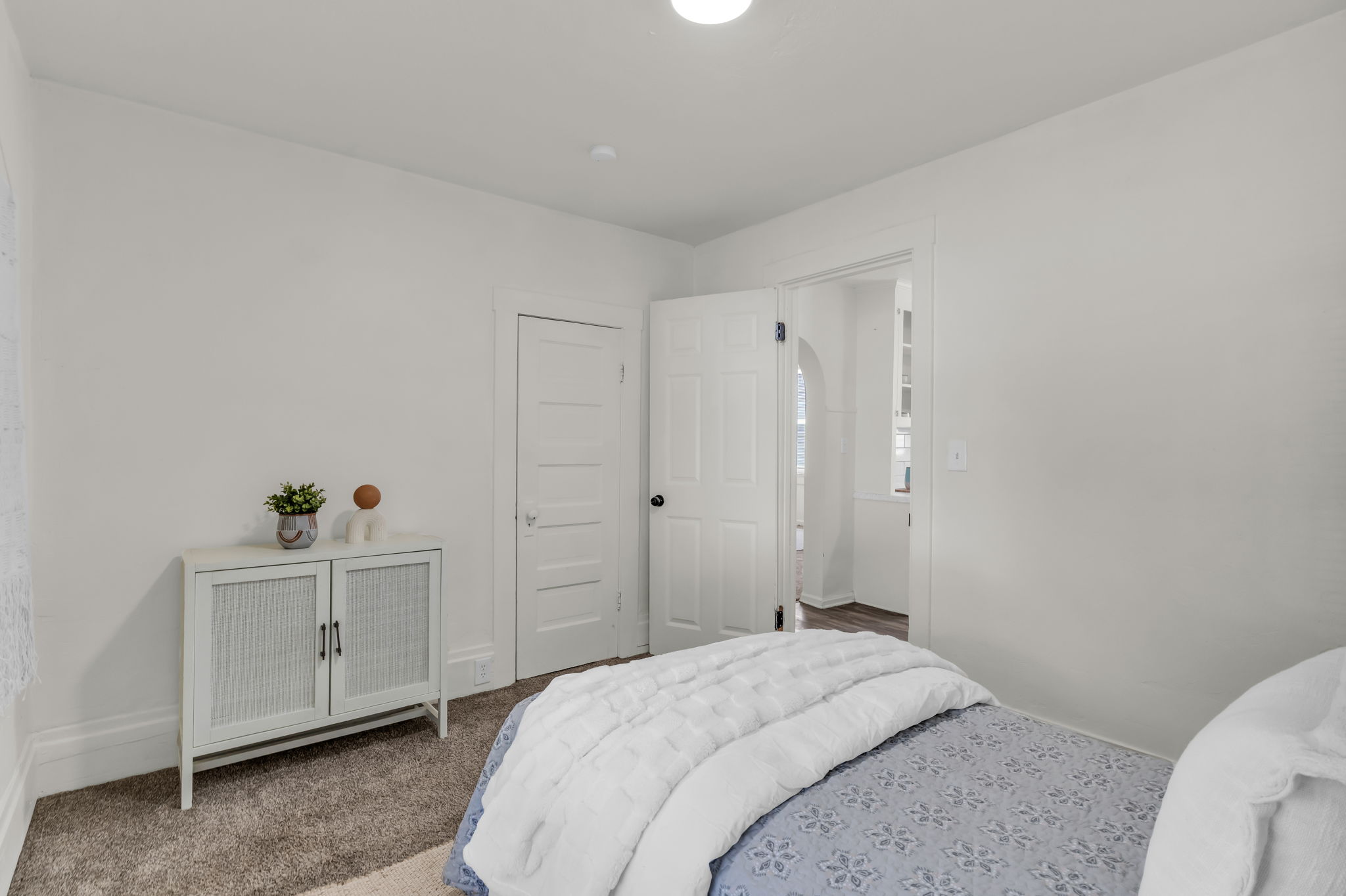 Carpeted room with a white door and an arched doorway revealing a separate space