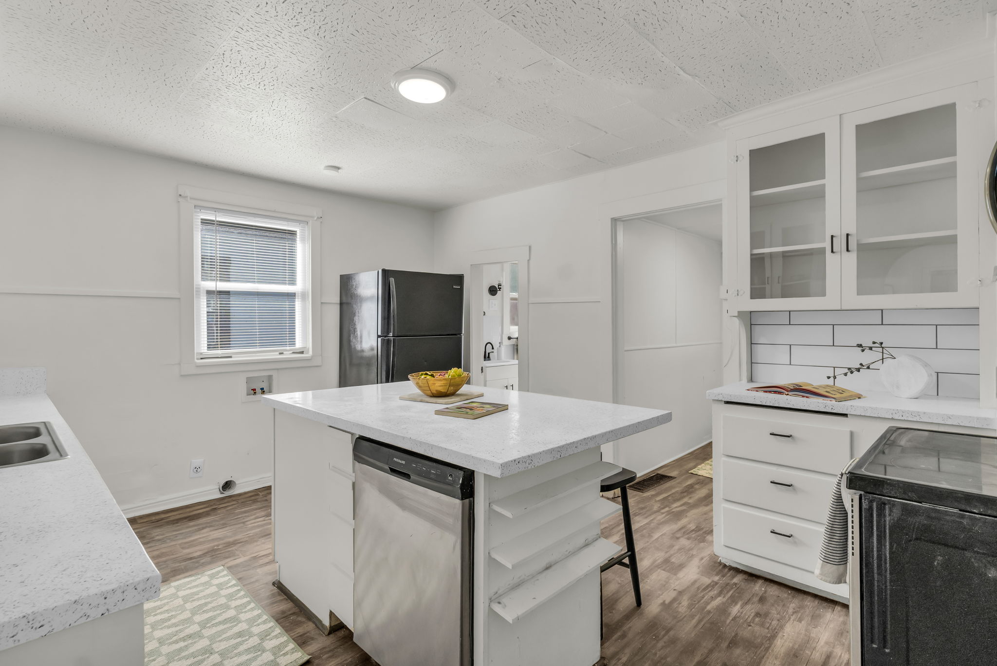 Bright kitchen featuring a central island with a built-in dishwasher, white countertops, a double basin stainless steel sink, and wood-finish flooring