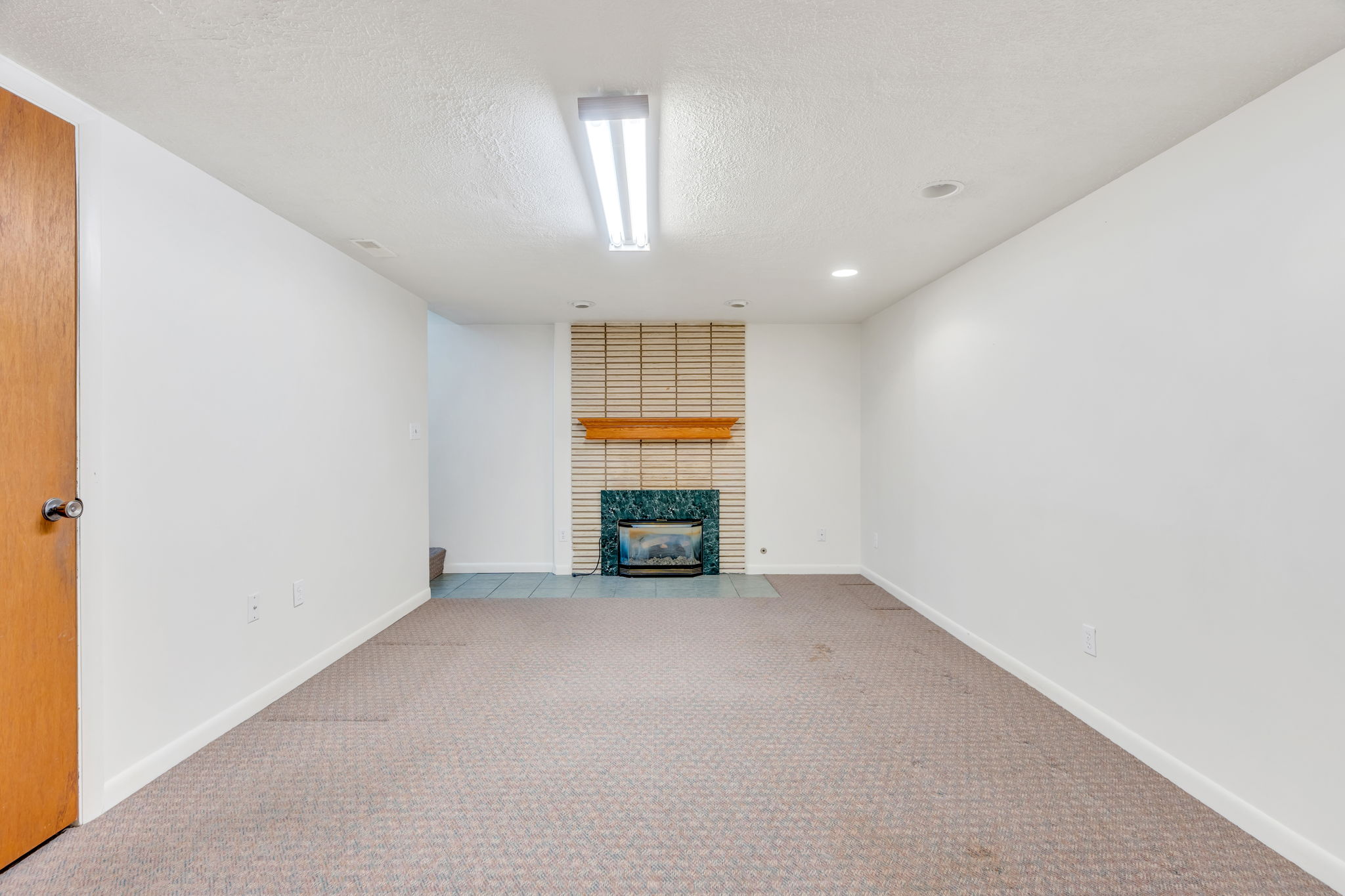 Carpeted room featuring a fireplace with a wood mantle, green-toned tile surround, and horizontal textured tile accent wall